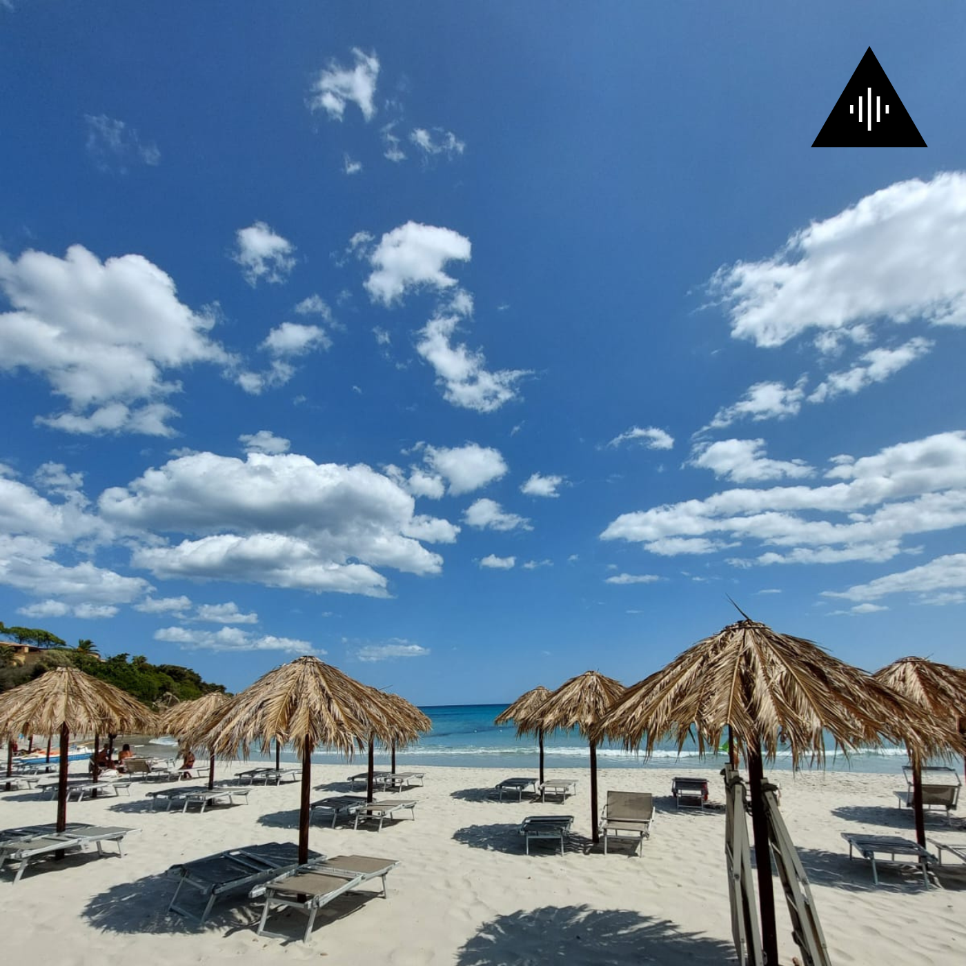 Empty beach with straw umbrellas and lounge chairs, blue sky with scattered clouds, ocean in the background.