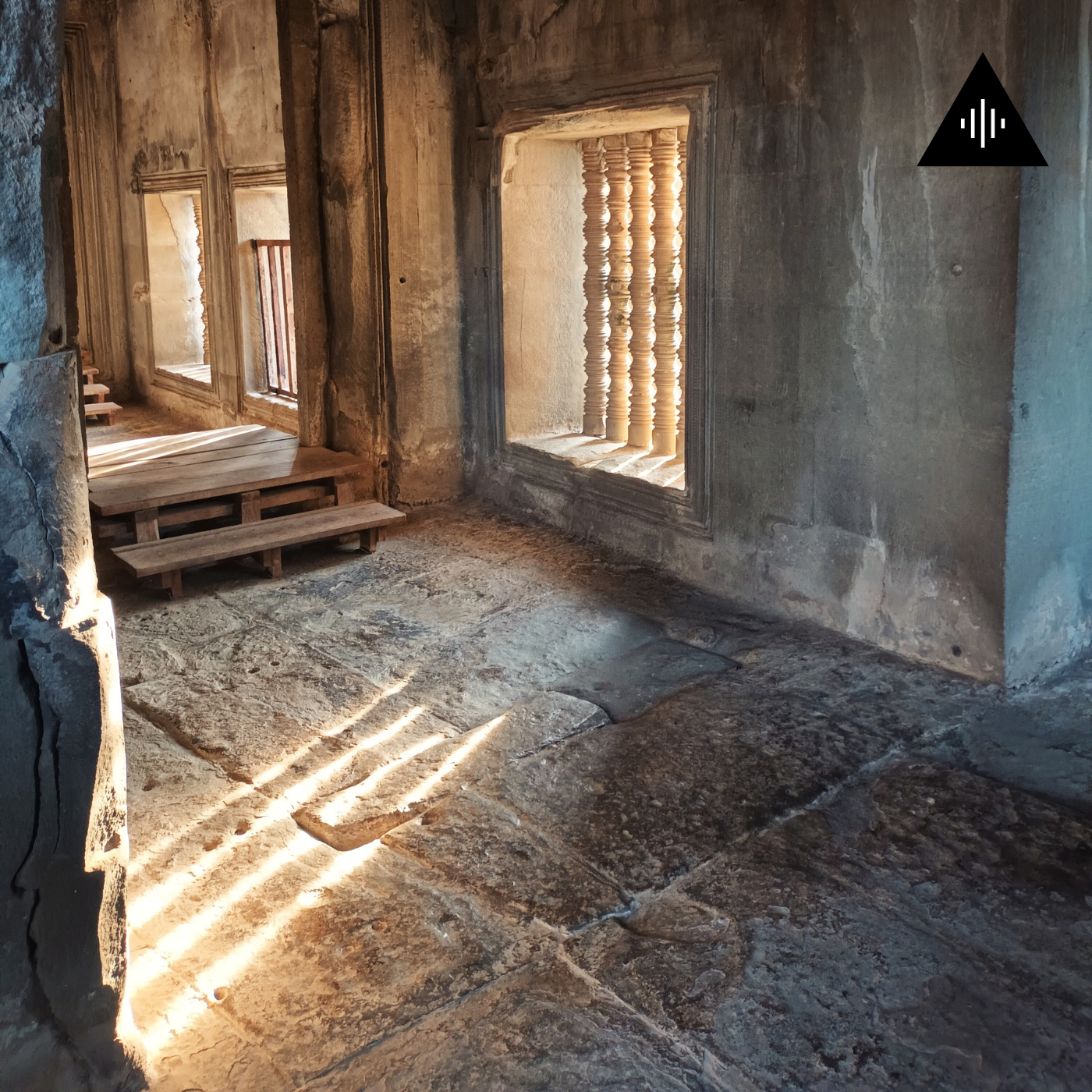 Sunlight streams through a window with decorative wooden bars, illuminating an old stone floor in a rustic, weathered stone and wood interior.