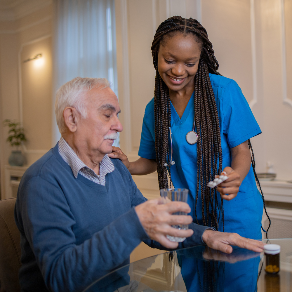 A nurse assisting an elderly man with taking medication at a dining table.