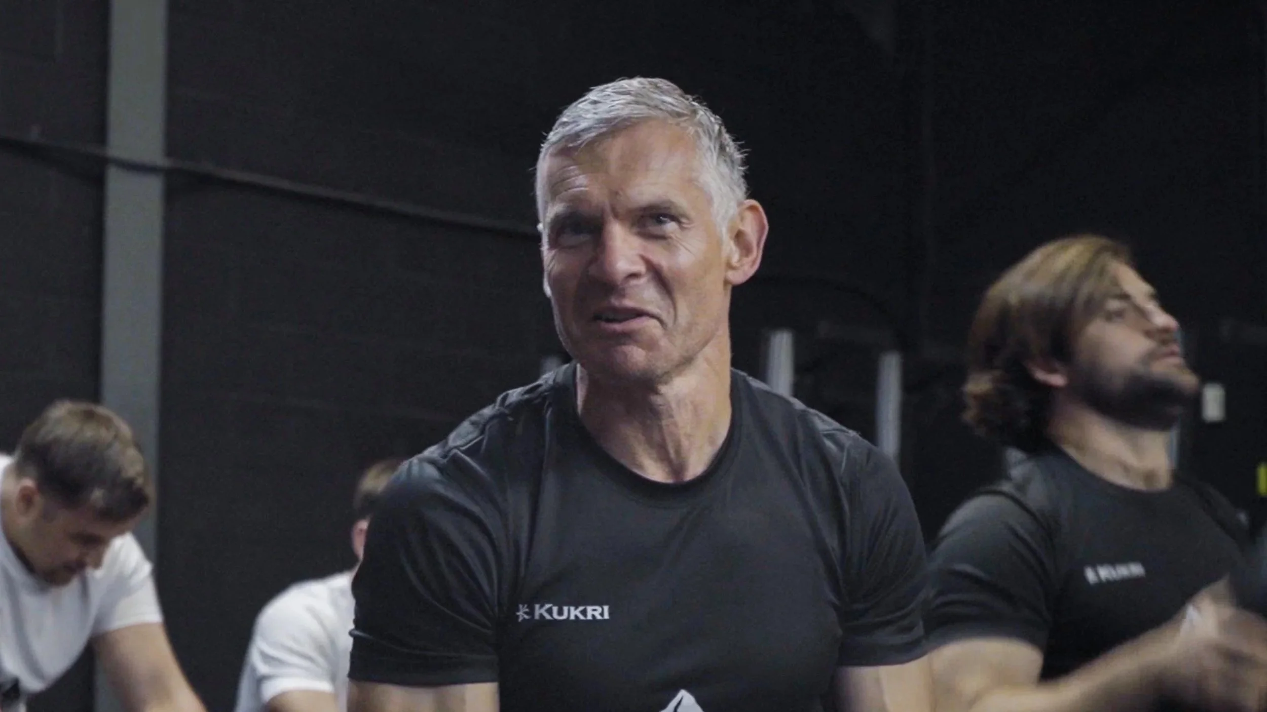 Group of hikers walking on a trail in a rural landscape, some wearing jackets, with a man in front carrying a map.