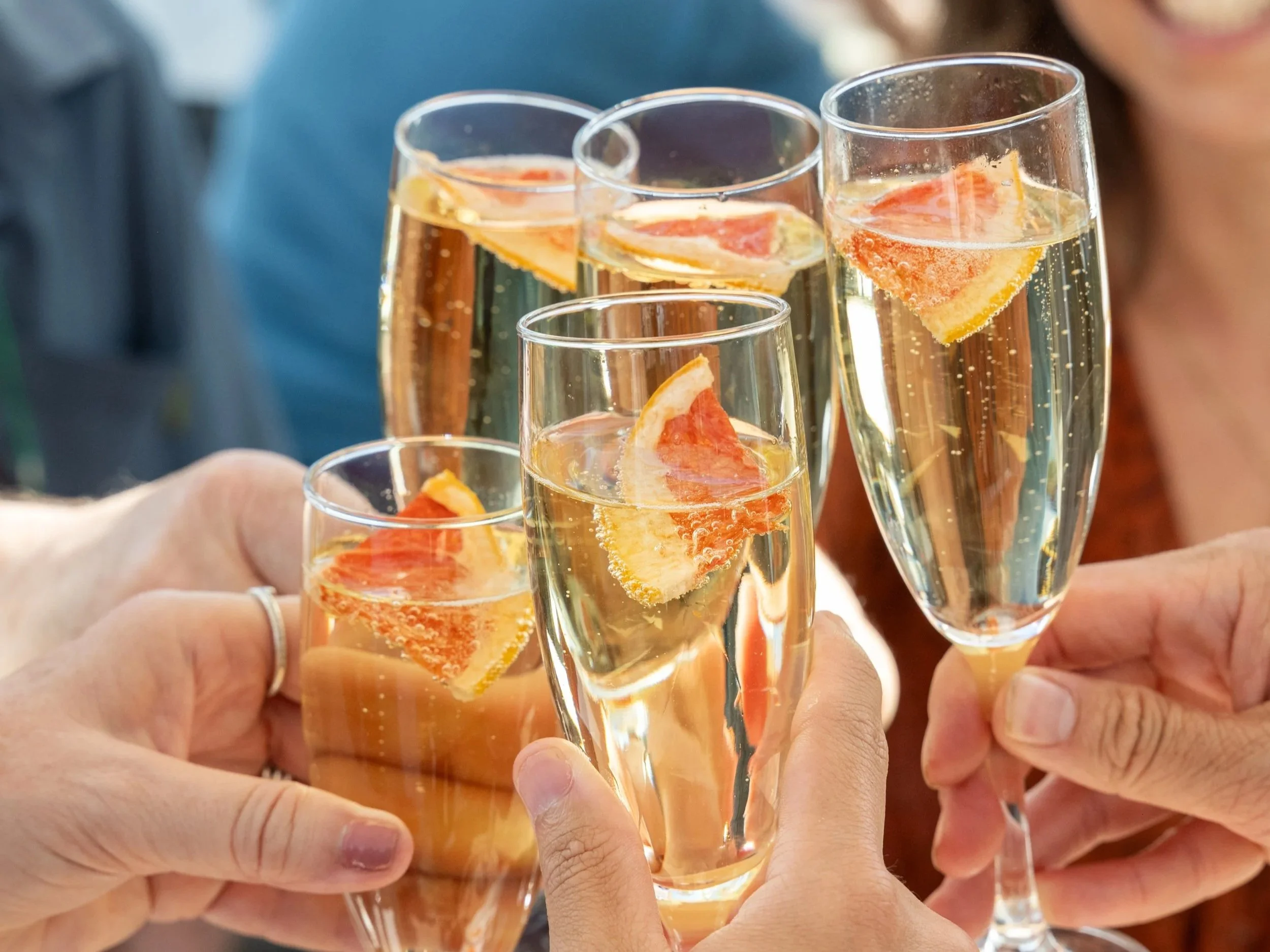 People raising glasses of champagne with slices of grapefruit inside for a toast.