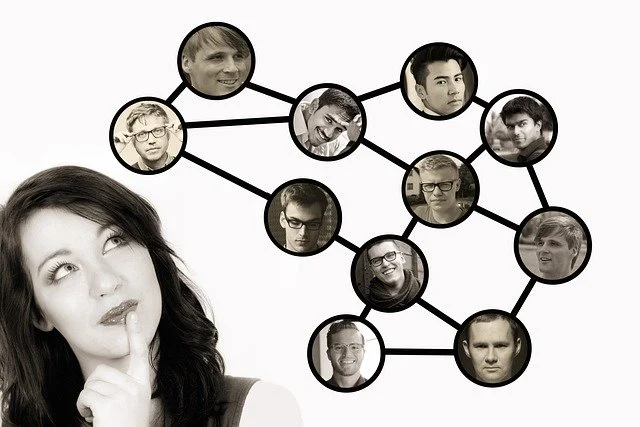 A woman with dark hair looking thoughtful, with her finger on her lips, in front of a network diagram of interconnected black-and-white headshots of various people.