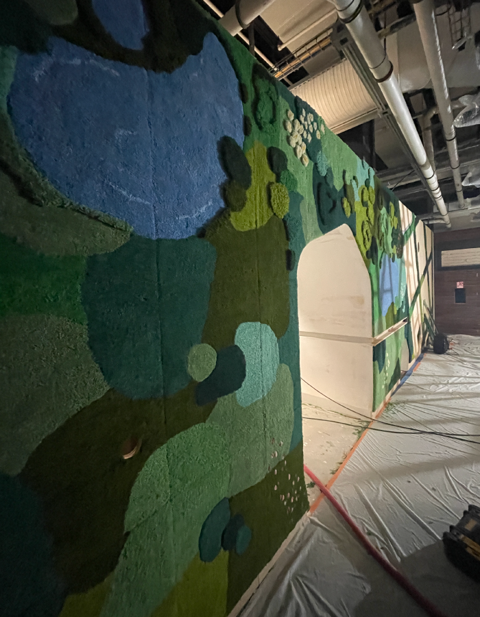 A colorful mural under construction: landscape scene featuring a pond, trees, hills, and greenery.