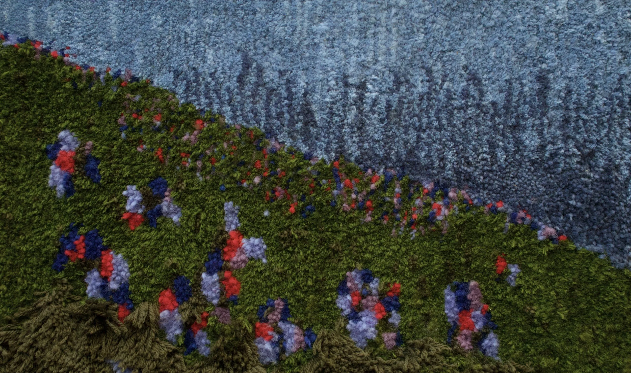 Close-up of a textured wall with a mural of a green hill with colorful flowers, overlapping a sky background with a pattern of small blue dots.