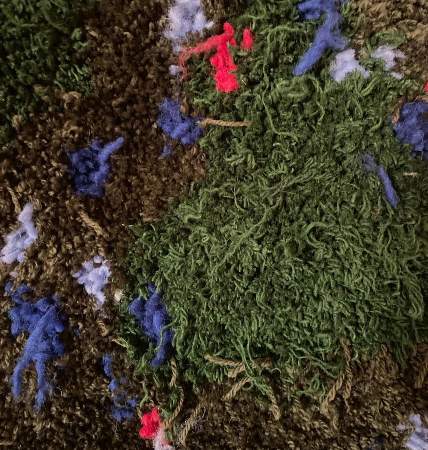 Close-up view of a surface made of dried plant material with colorful yarn or thread decorations, including red, blue, white, and green strings.