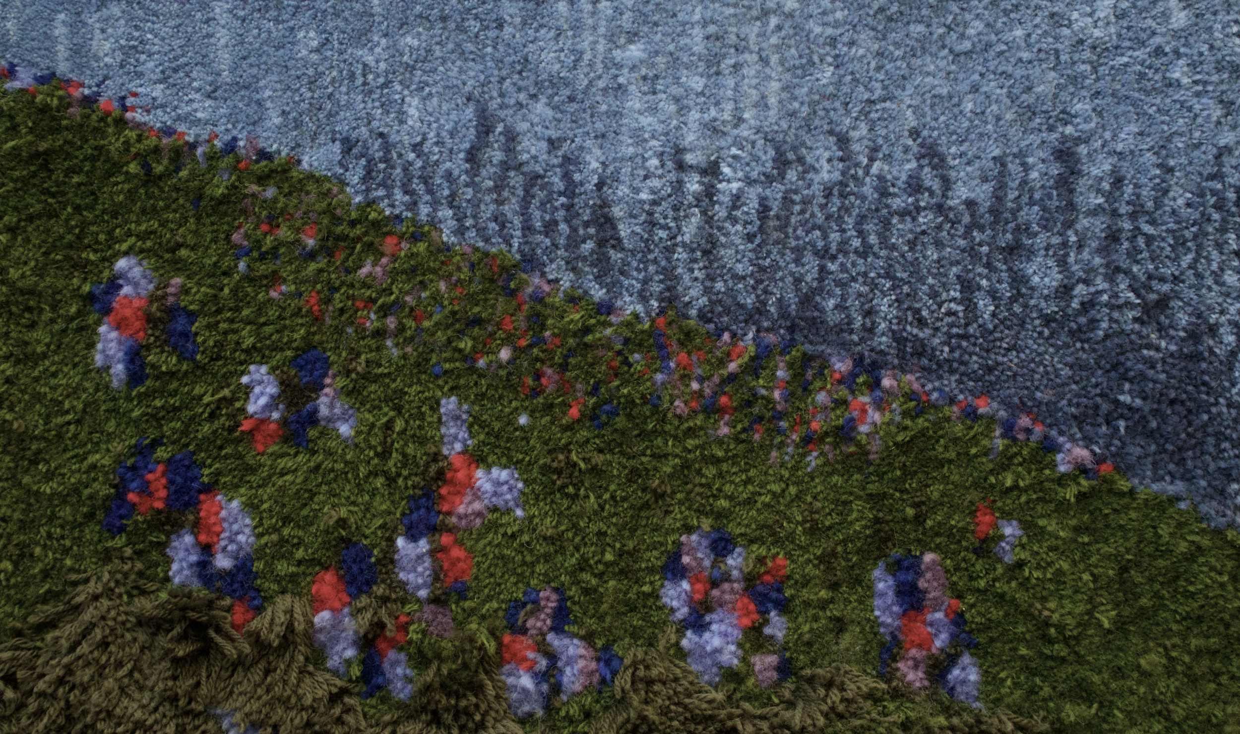 Close-up of a colorful floral embroidery on fabric, showing green leaves and red, blue, pink, and purple flowers against a textured blue background.