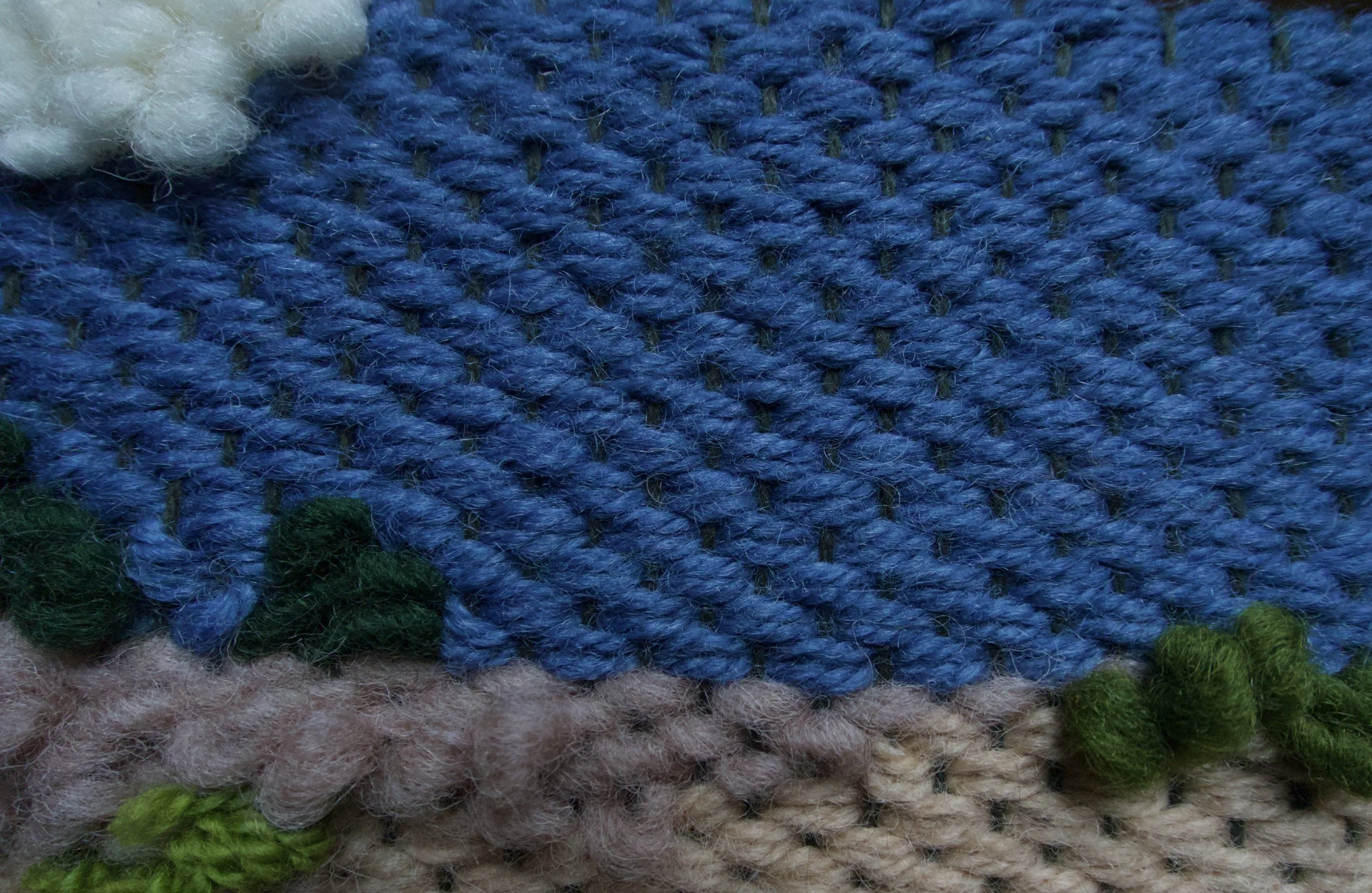 Close-up of a textile with layered yarn in blue, tan, green, and white colors.