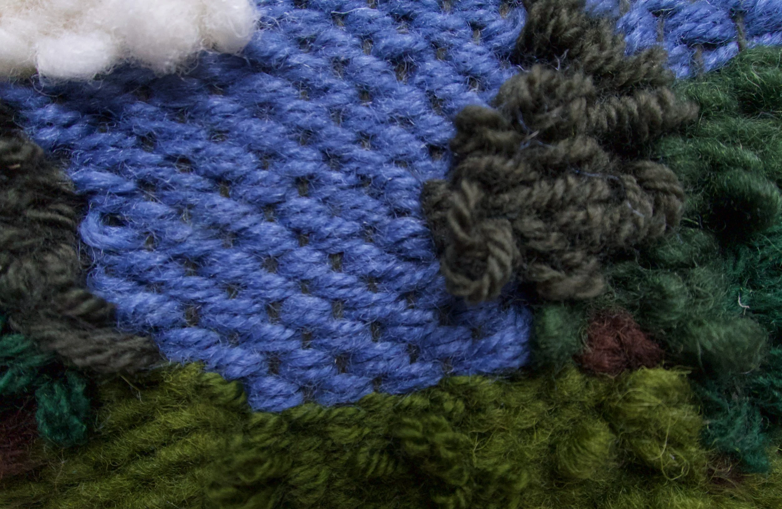 Close-up of multicolored yarn or fabric strands, including blue, green, black, white, and brown woven textures.