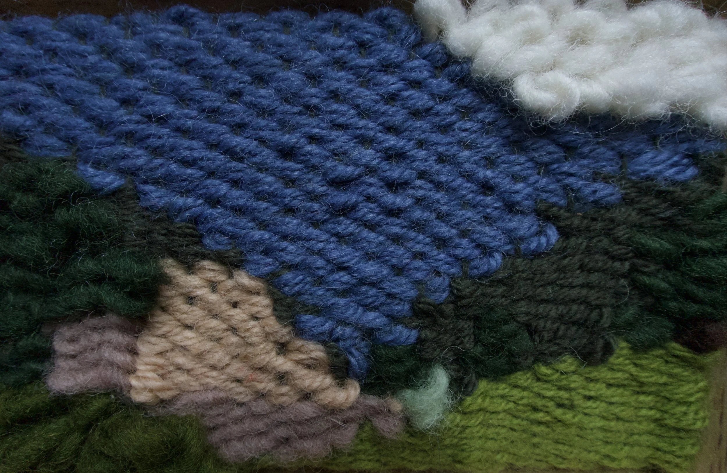 Close-up of colorful knitted yarns in shades of blue, beige, gray, and green.