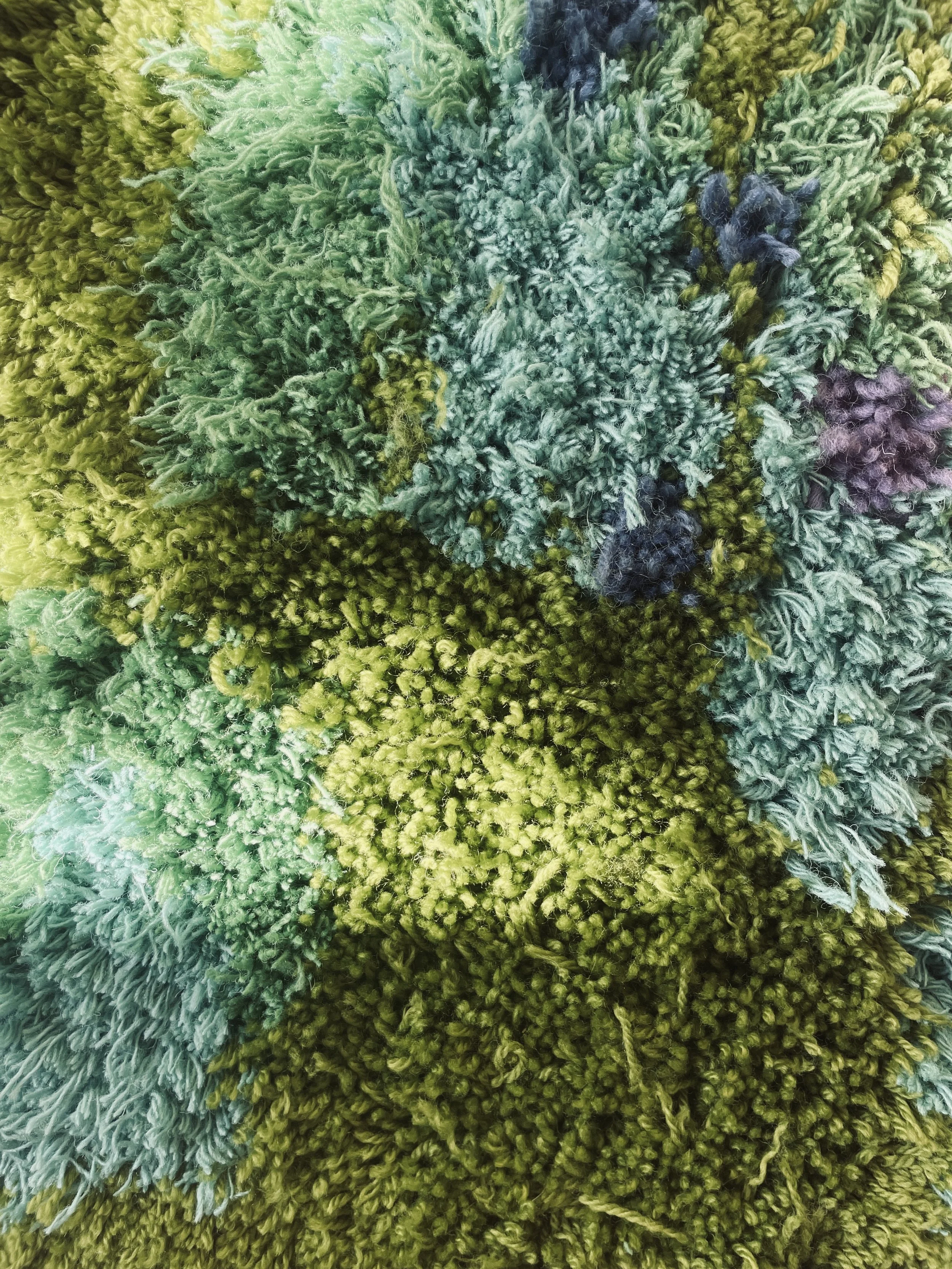 Close-up of a multicolored shaggy rug with various shades of green, blue, and purple fibers.