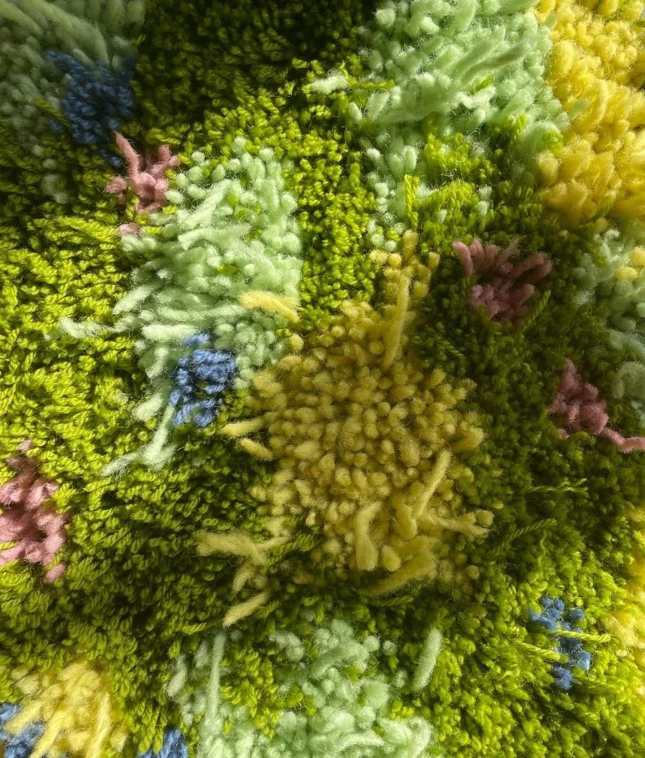 Close-up of a multicolored textured surface, possibly a macrame or textile with a variety of green, yellow, pink, blue, and white fibers.