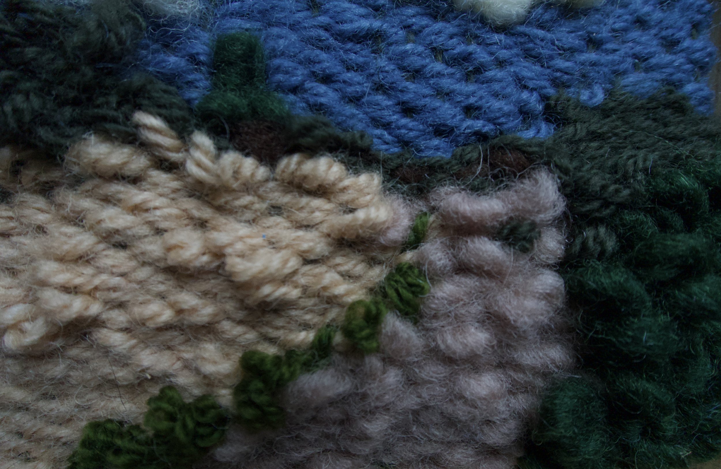 Close-up of various colorful yarns, including blue, beige, green, and dark colors, arranged together.