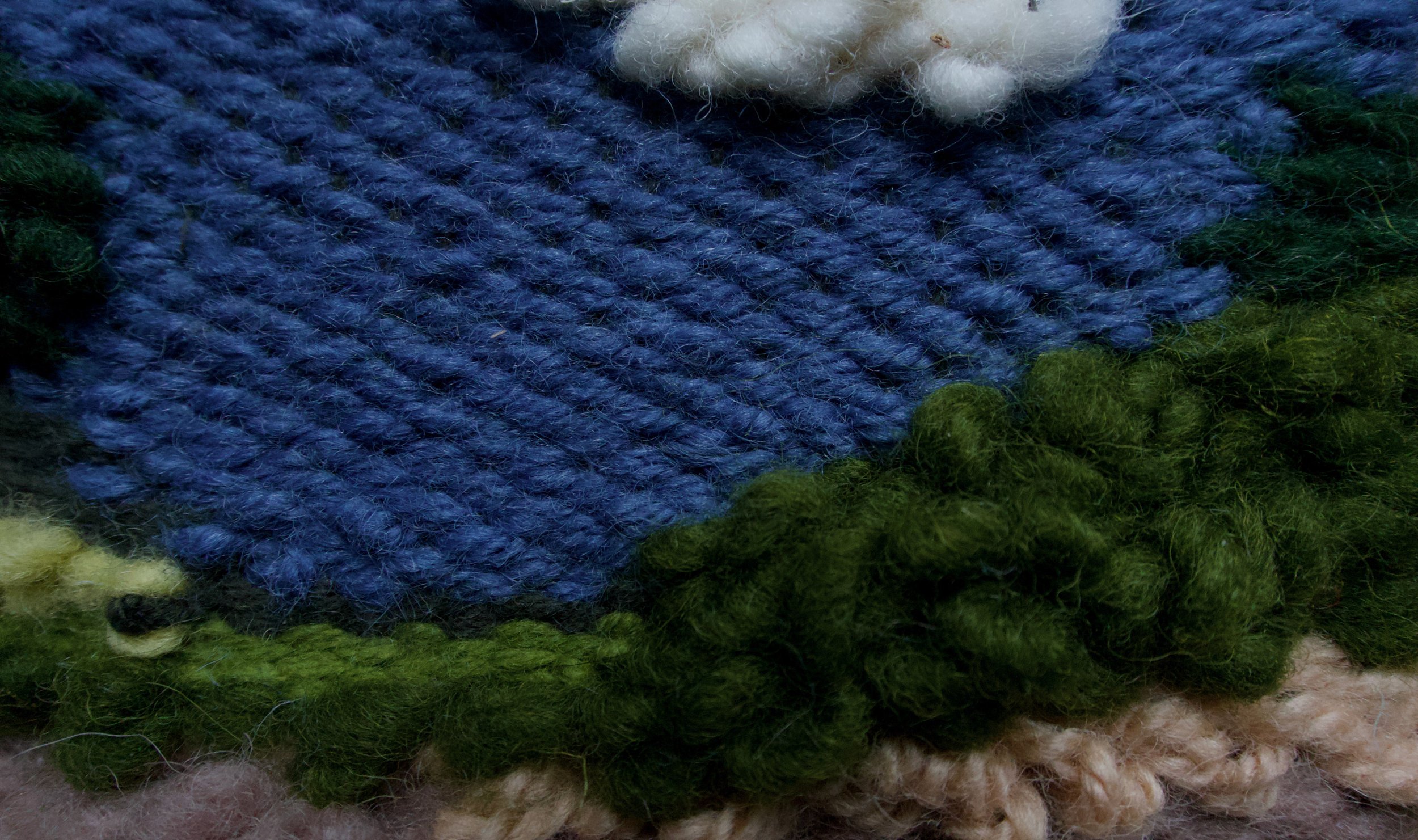 Close-up of multi-colored, textured wool or yarn, including blue, green, white, black, yellow, and pink fibers.