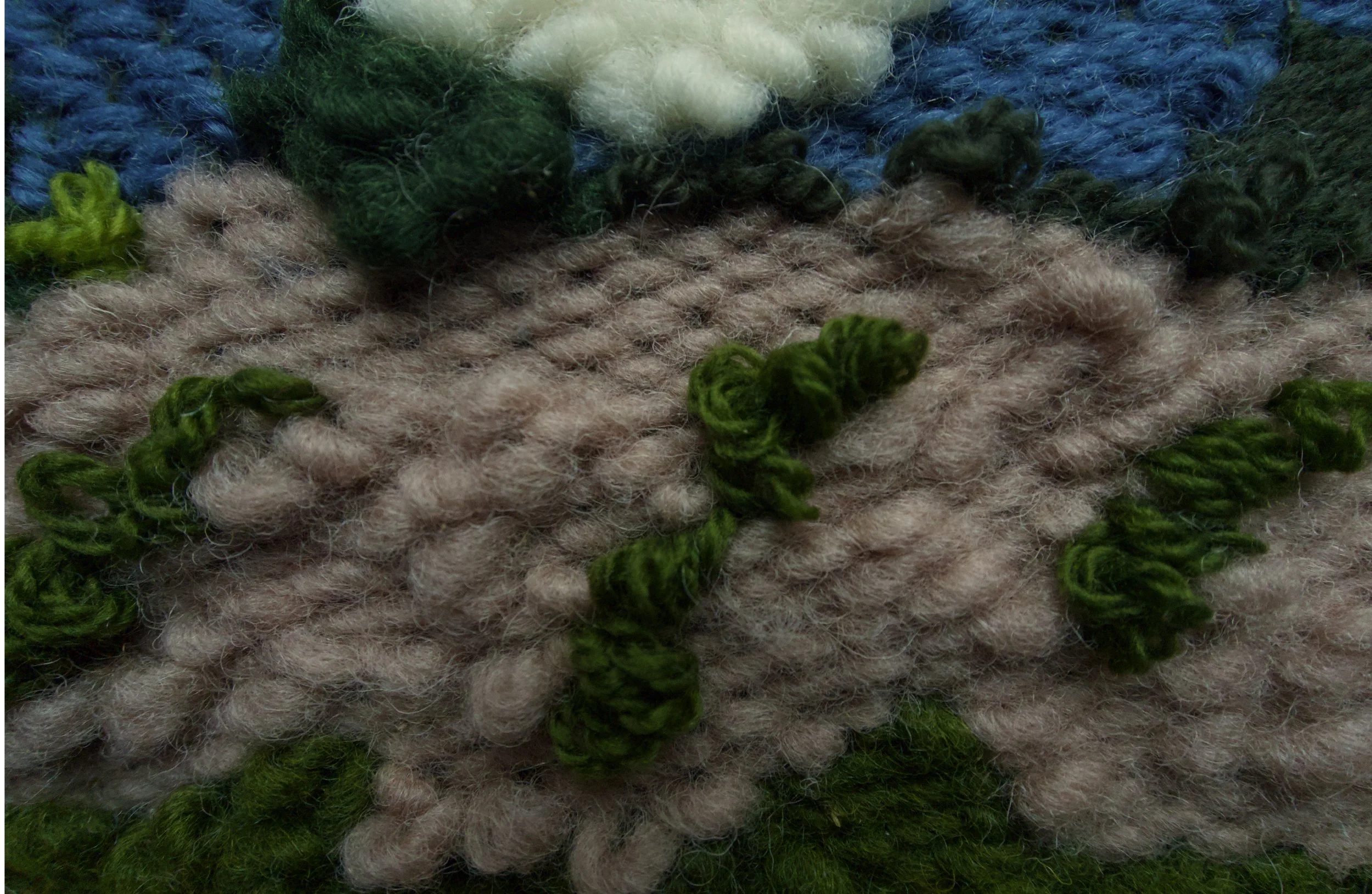 Close-up view of multi-colored wool yarns, featuring beige, green, blue, and white hues, arranged in overlapping strands.