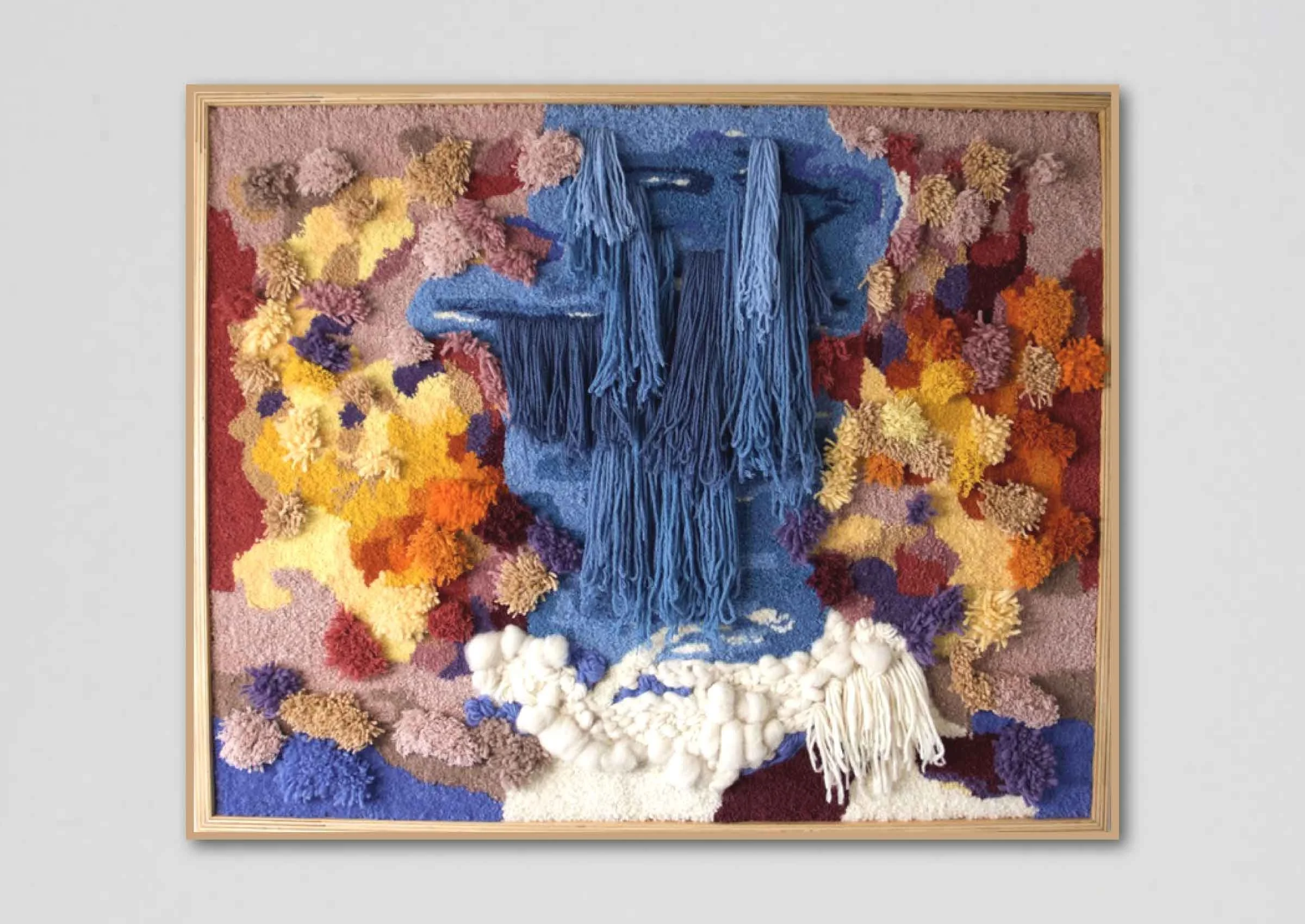 Textured wall art featuring a blue waterfall made of yarn surrounded by colorful yarn flowers in shades of pink, yellow, purple, and white, framed in light wood.