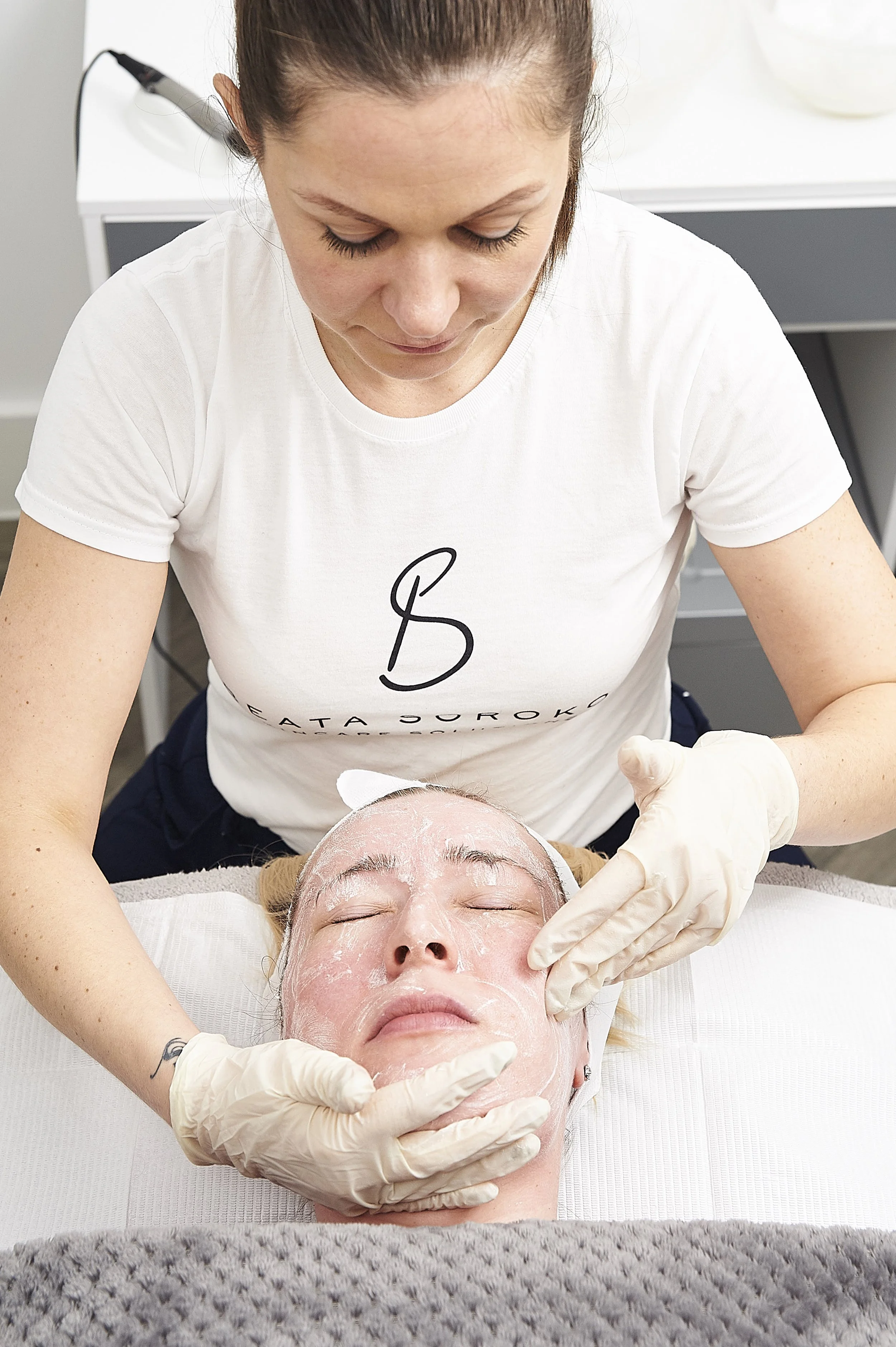 A woman receiving a facial treatment from an esthetician in a spa or skincare clinic.