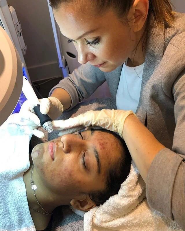 A dermatologist applies a treatment to a woman's face in a clinic setting.