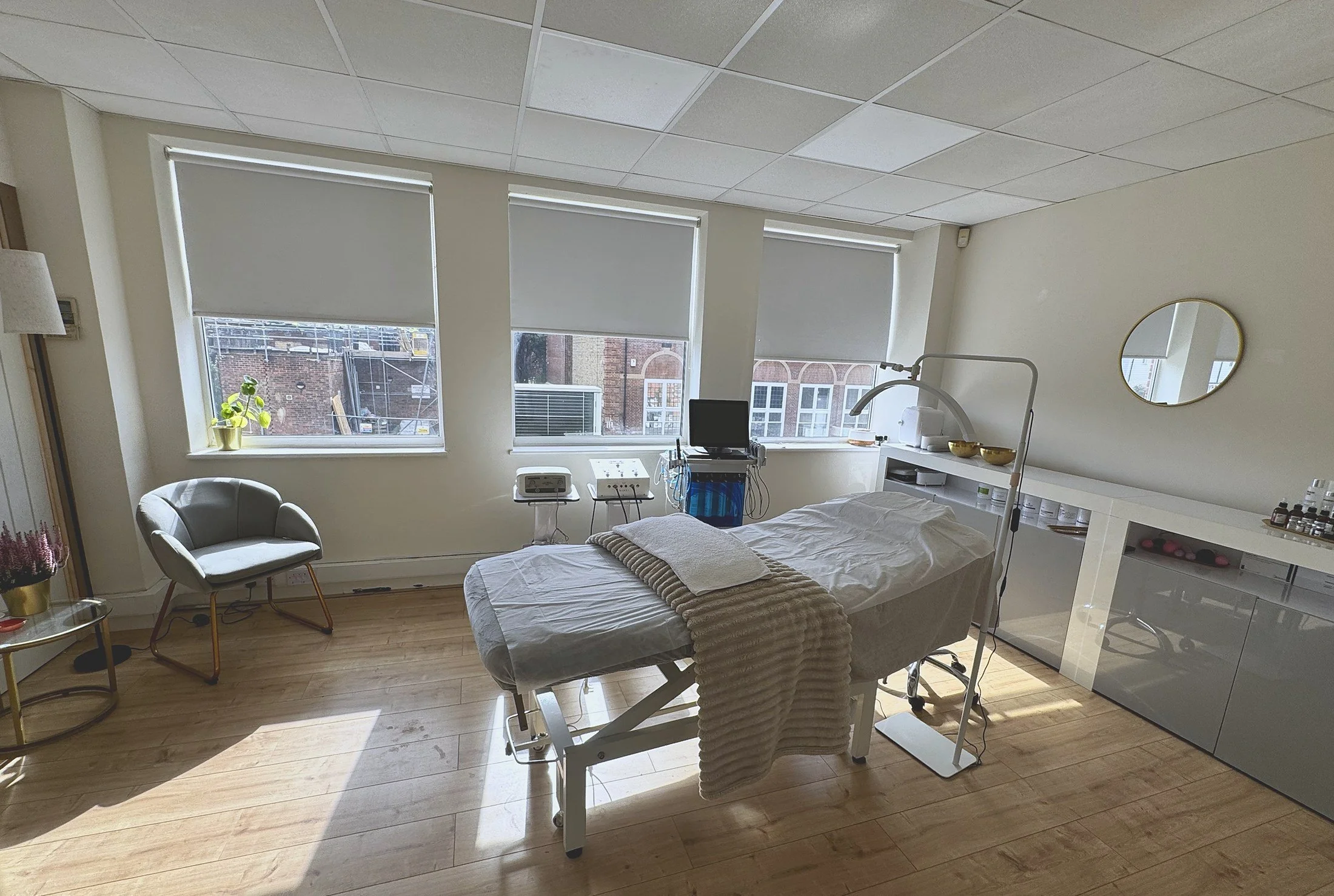 A skincare treatment room with a treatment bed covered in a white sheet, a large promotional poster on the back wall advertising Beara Soroko Skincare Solutions, and various skincare products and medical equipment on the counters.