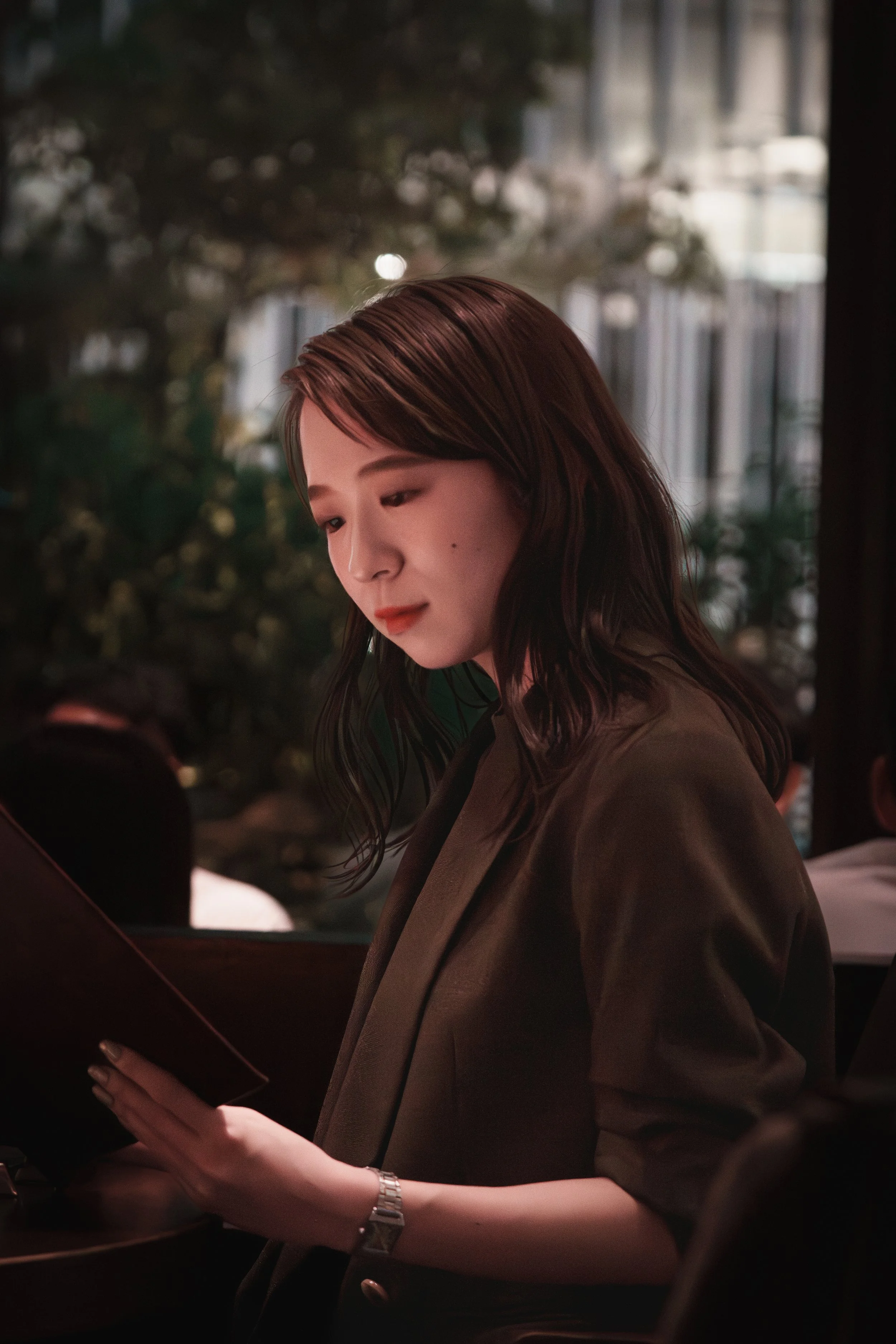 A young woman with shoulder-length brown hair reading a menu inside a dimly lit restaurant.