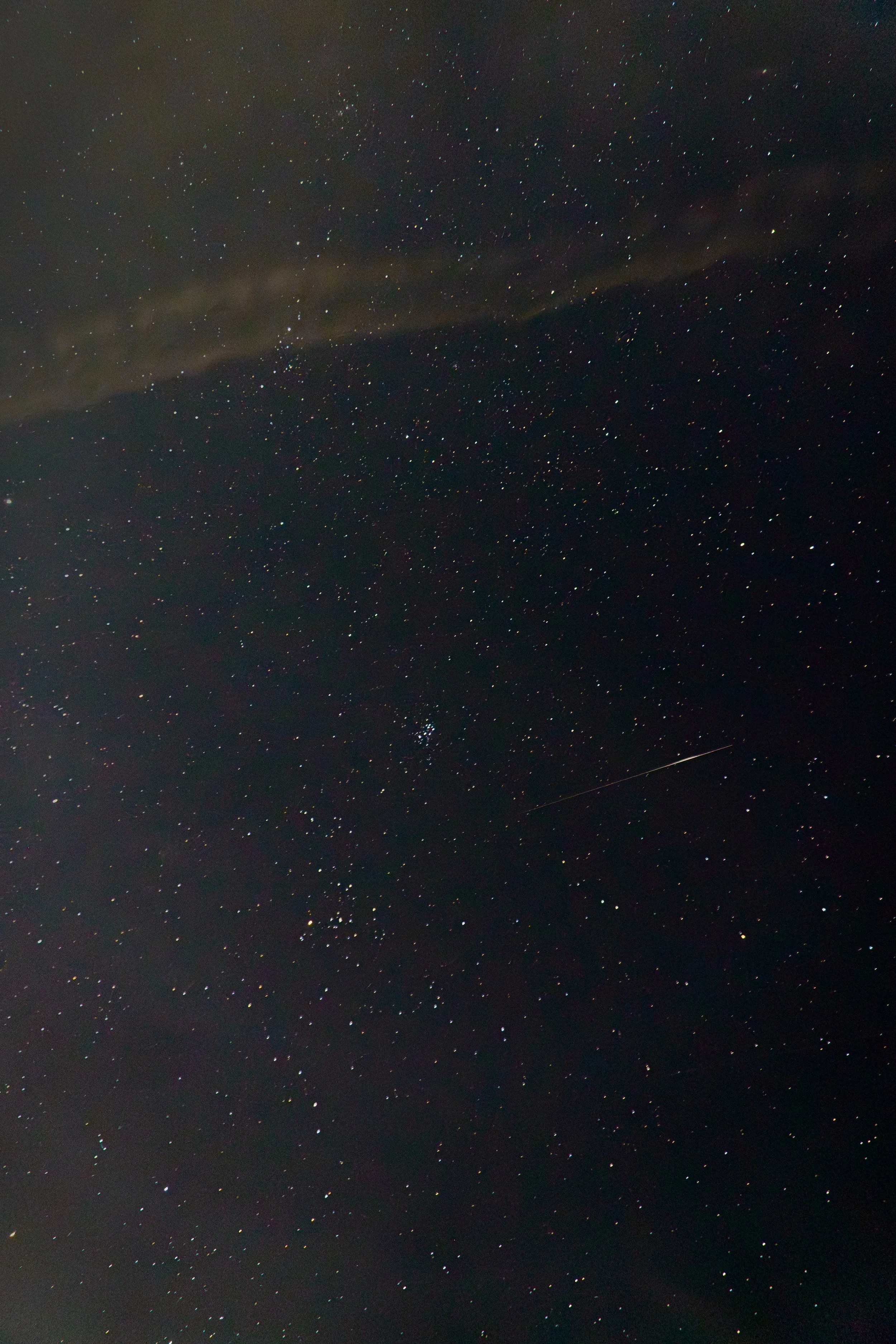 Night sky filled with numerous stars and a faint streak of a shooting star, with some clouds partially covering the sky.