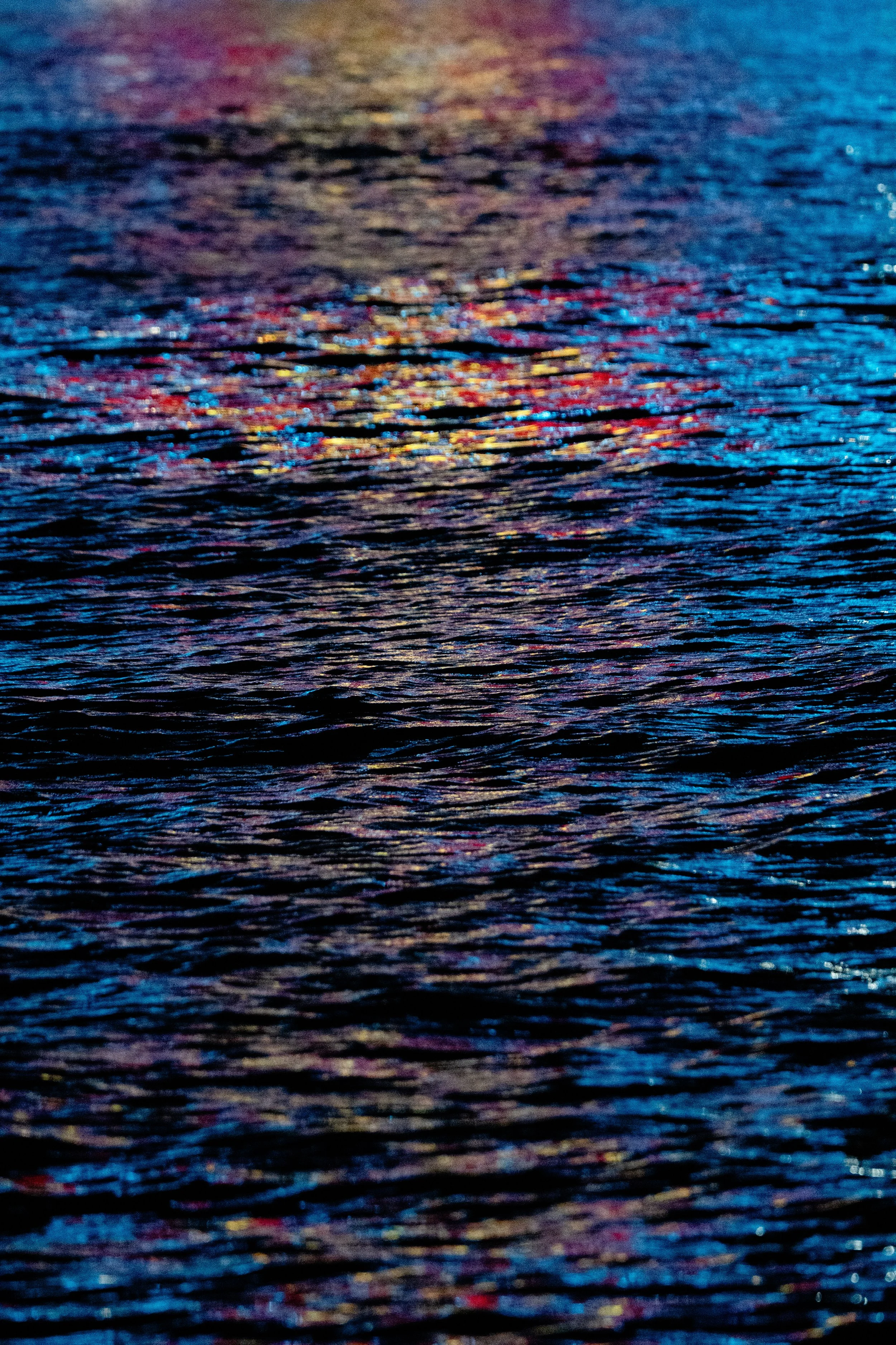 Colorful reflections on the surface of water, with shades of blue, purple, pink, and gold.
