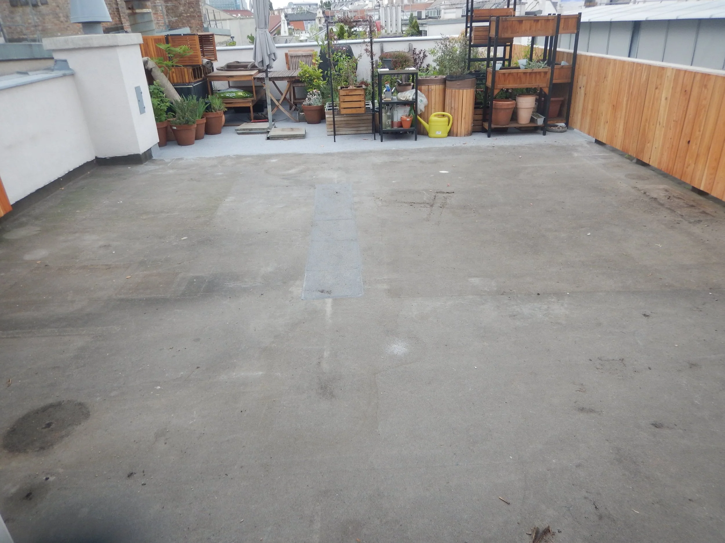 Ansicht der gesamten Terrassenfläche und aller schadhaften Stellen mit Möbel und Pflanztrögen im Hintergrund.