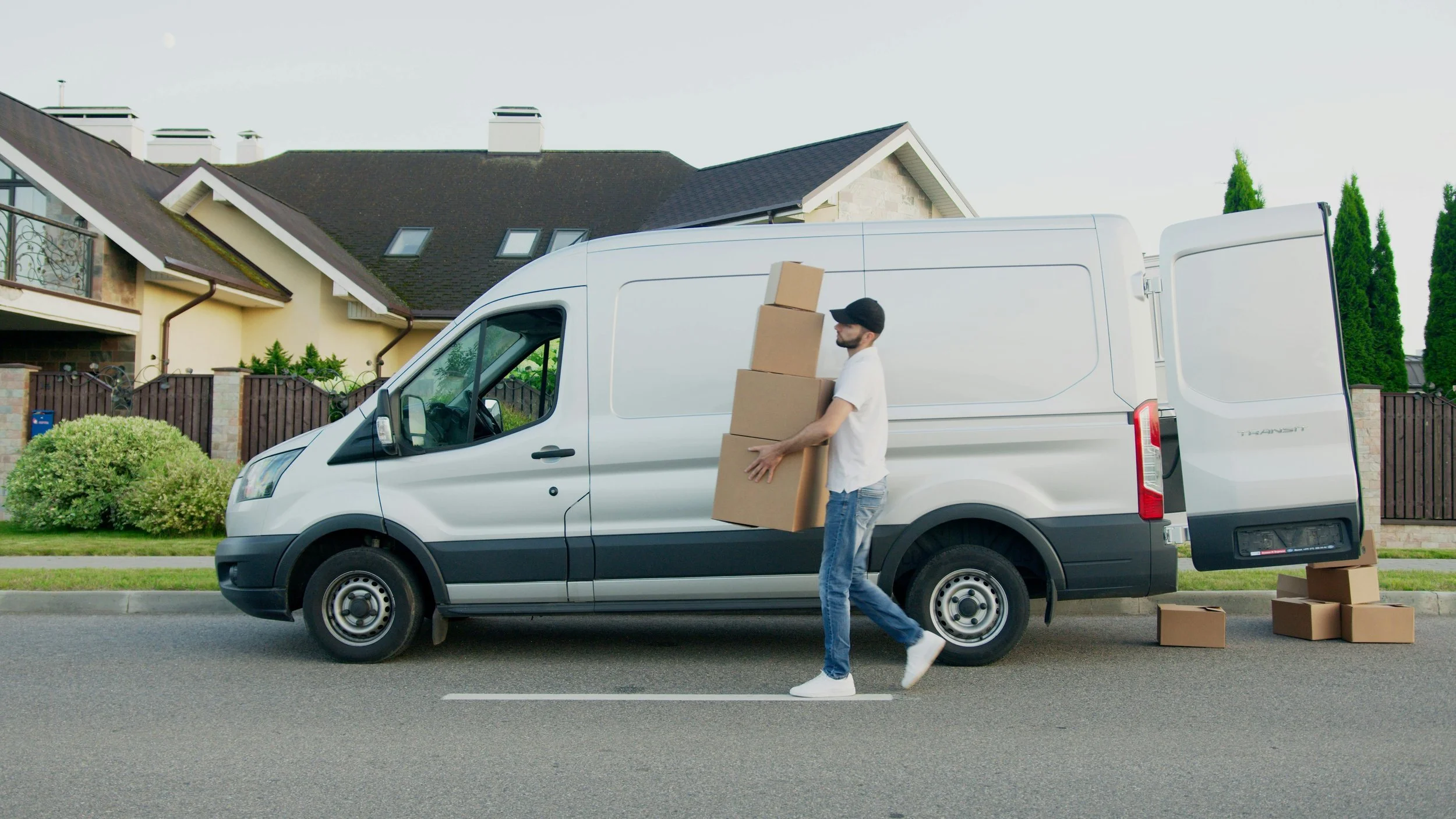 Un homme portant des cartons se trouve à côté d'un camion blanc stationné sur la rue, avec d'autres cartons au sol.