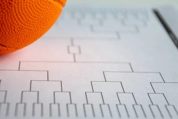 Close-up of a printed tournament bracket chart on paper with an orange billiard ball partially covering the top left corner.