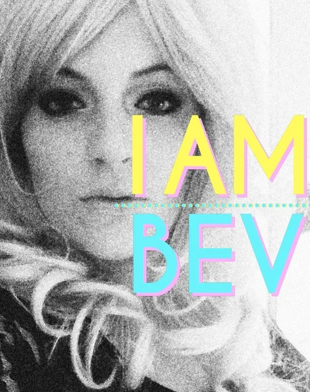 Black and white photo of a woman with long, wavy hair and dark eye makeup, with the colorful text "I AM BEV" overlaid.
