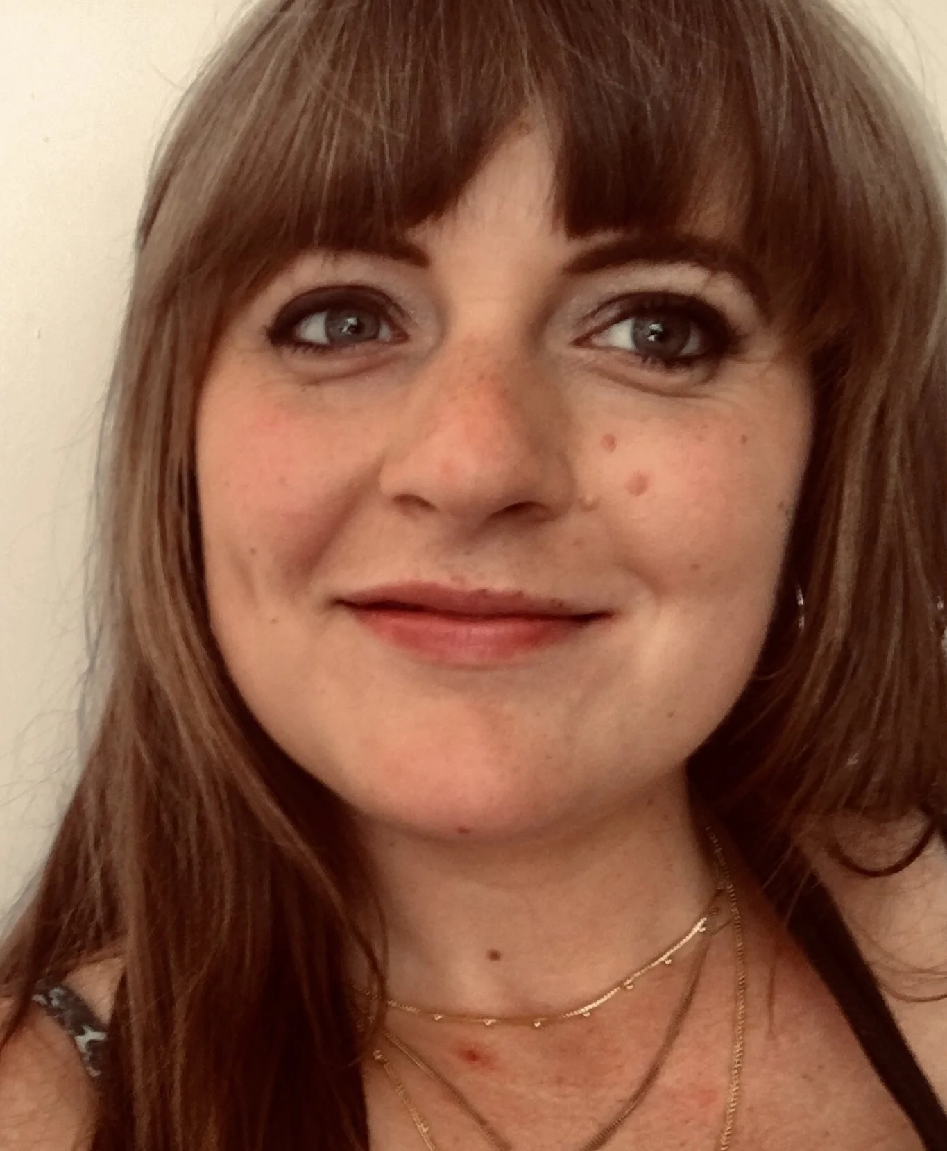 Close-up of a woman with reddish brown hair, blue eyes, and freckles, smiling slightly against a plain background.