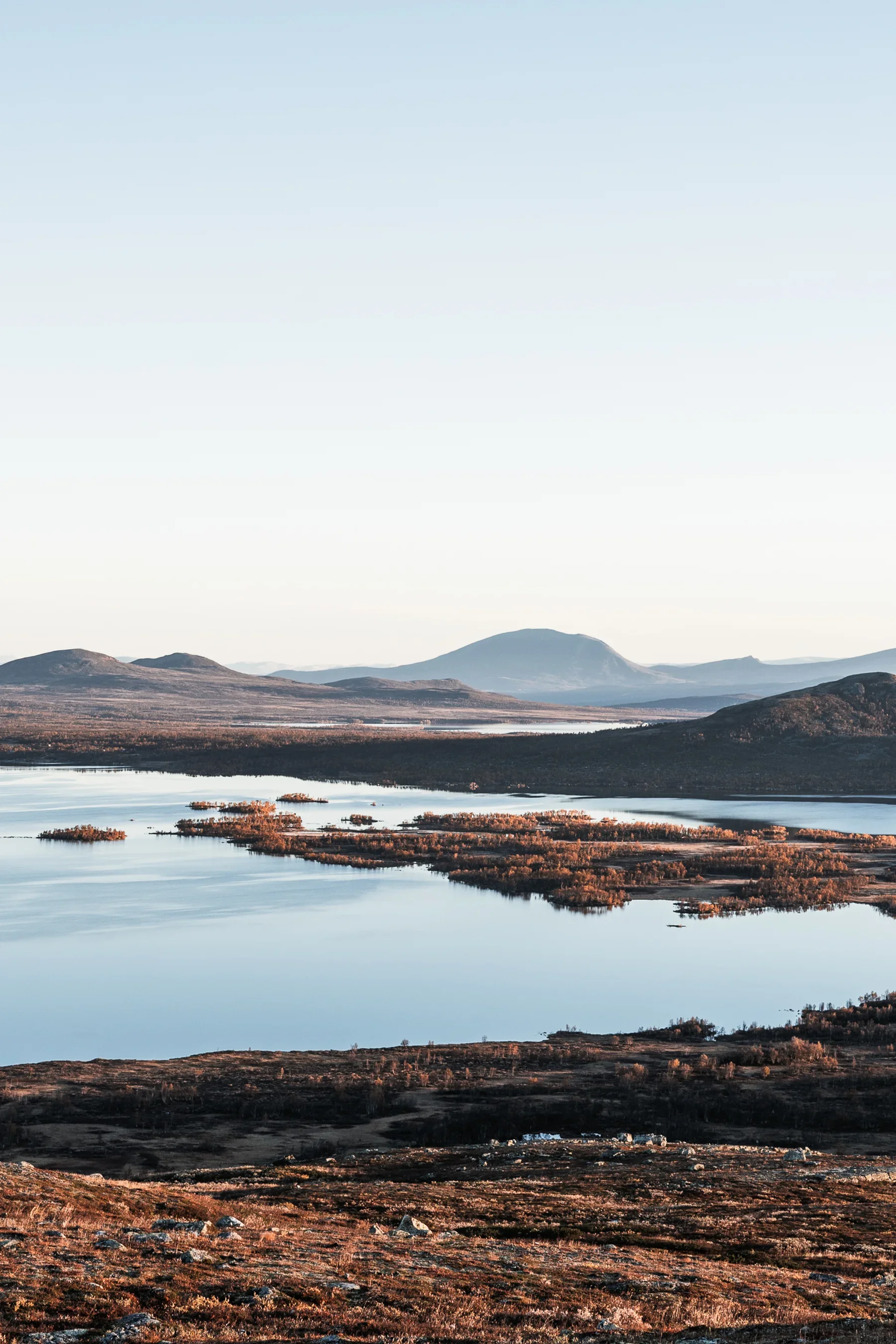 A landscape photo of a big lake with some tree covered islands in the foreground and some round mountains in the distance
