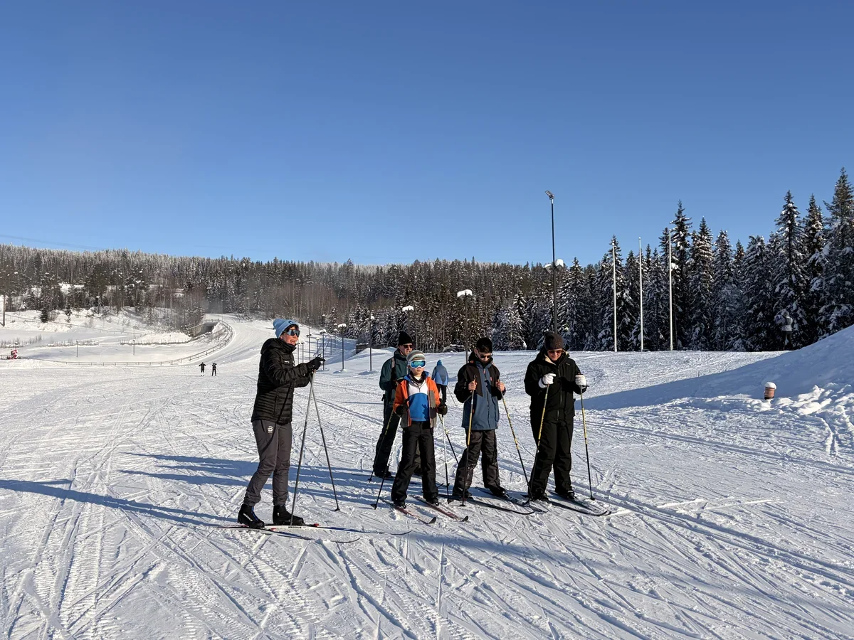 a family of four attending cross country skiing lessons. The teacher is standing next to them explaining technique.