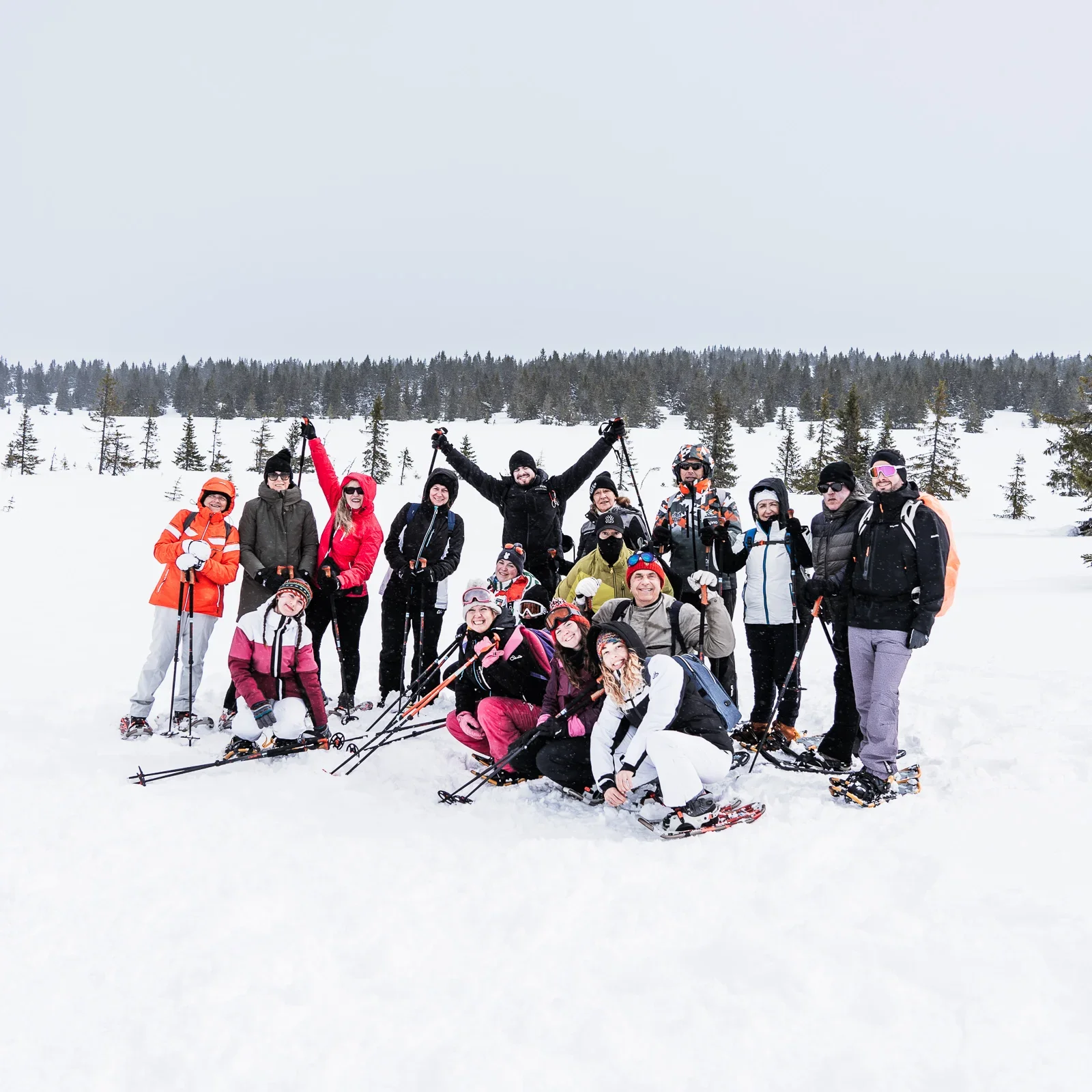 A group of people on snowshoes standing grouped together to pose for a group photos in front of a snow covered plain. Everyone is smiling, some are lifting their arms to cheer.