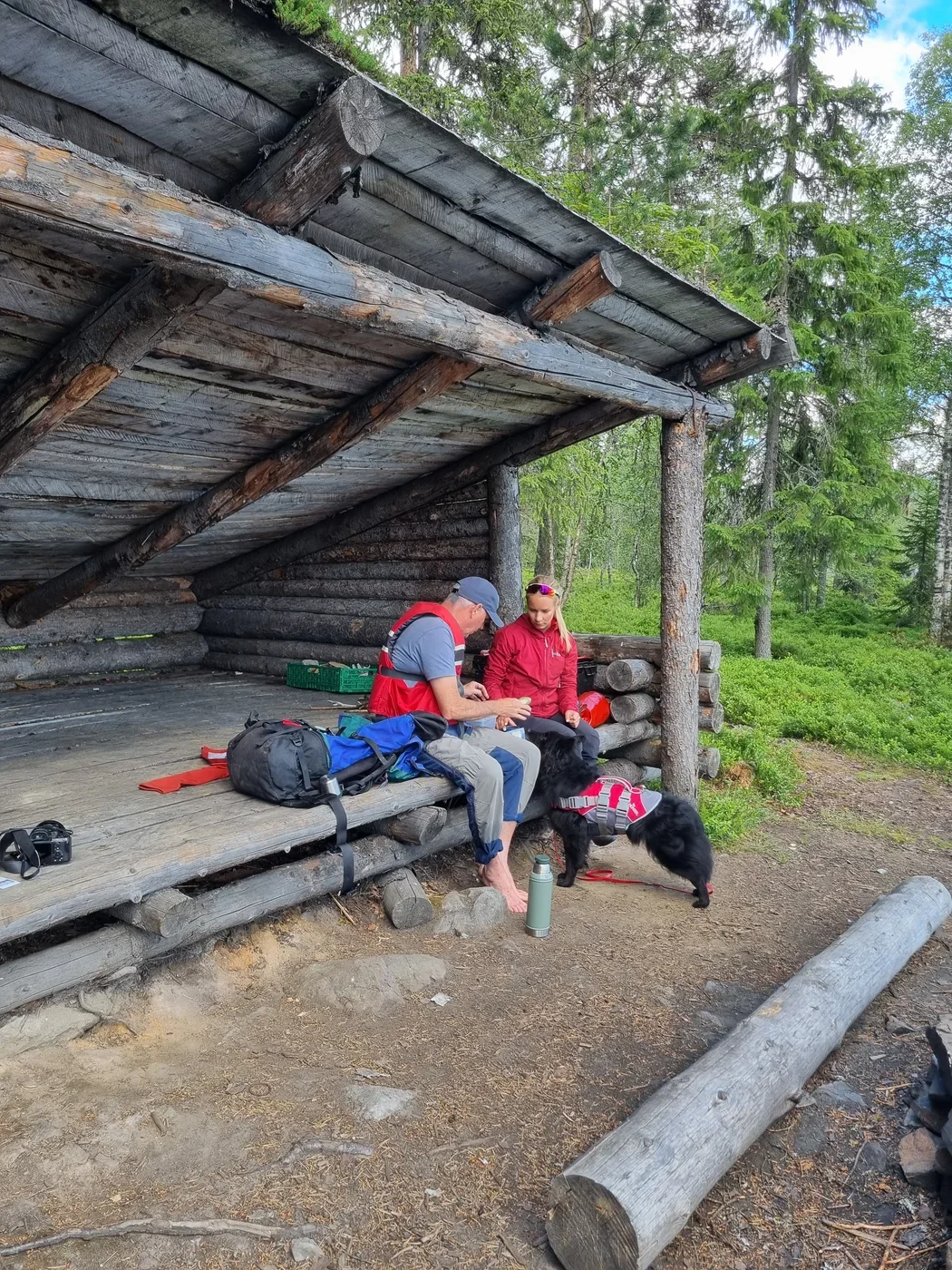 Two people in outdoor clothing sitting in a wooden shelter in the forest.