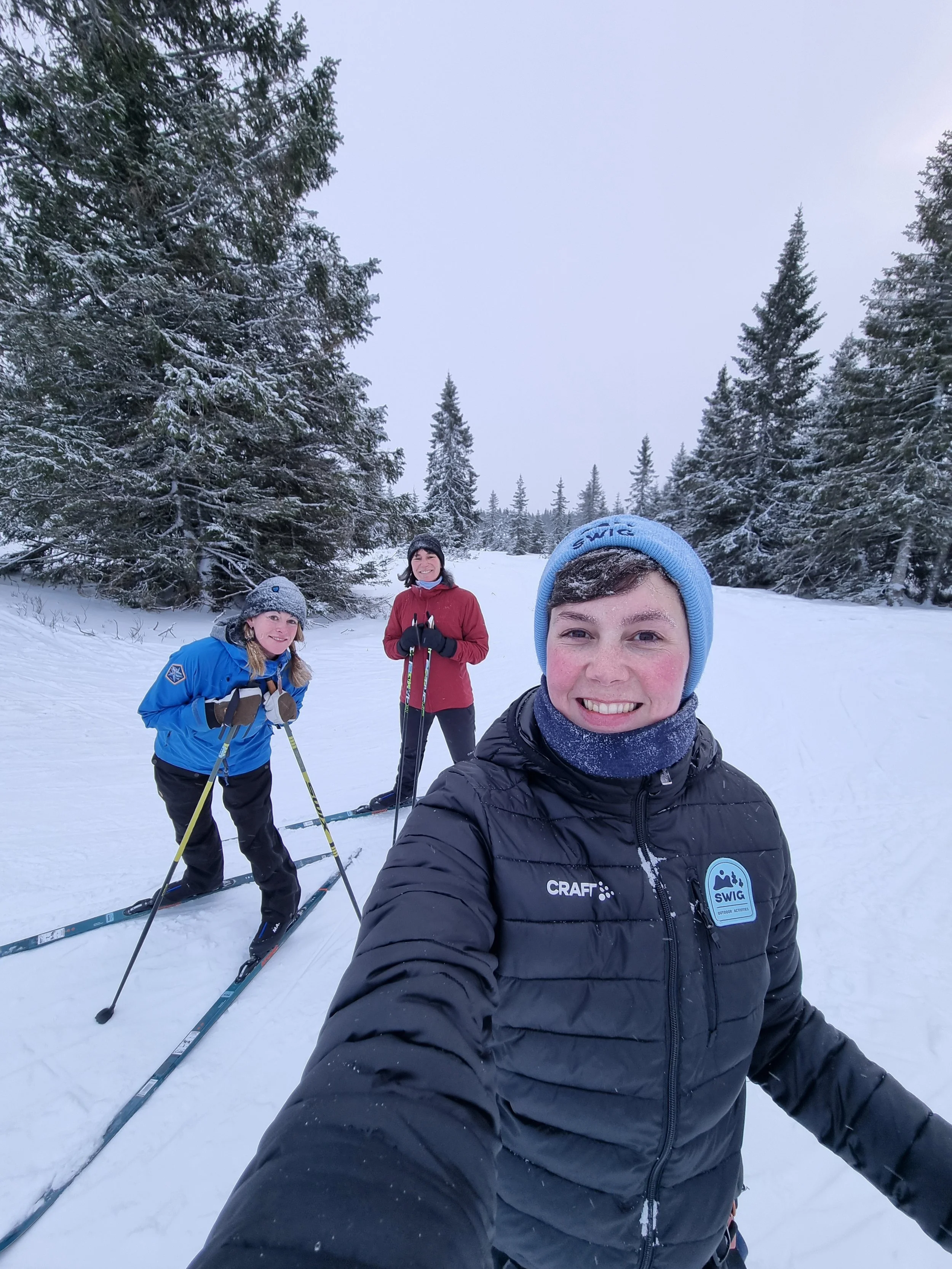 a selfie of three women crosscountry skiing, one person is taking the selfie, the other two are seen in the background