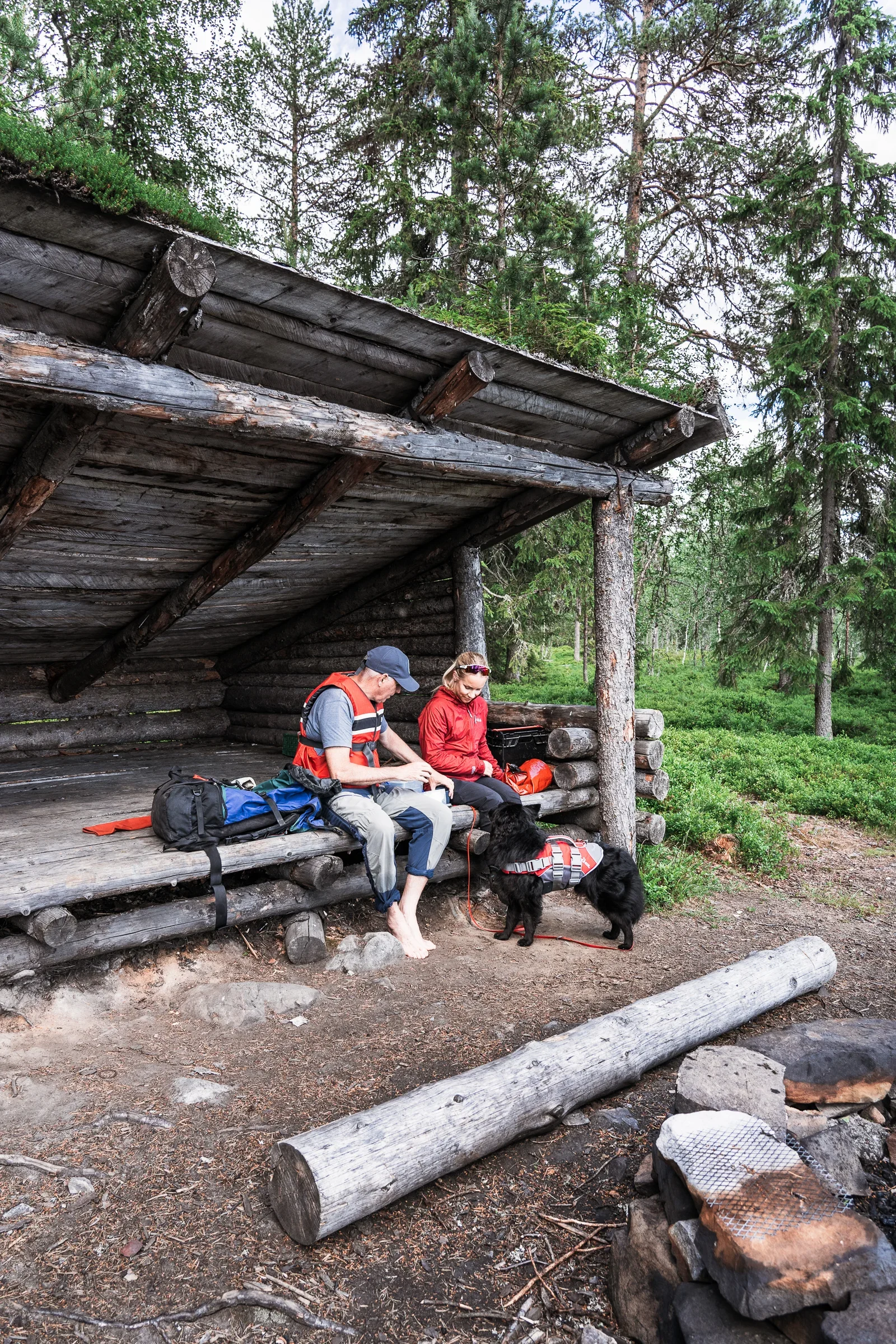 Two people sitting in a wooden shelter in the forest enjoing some snacks