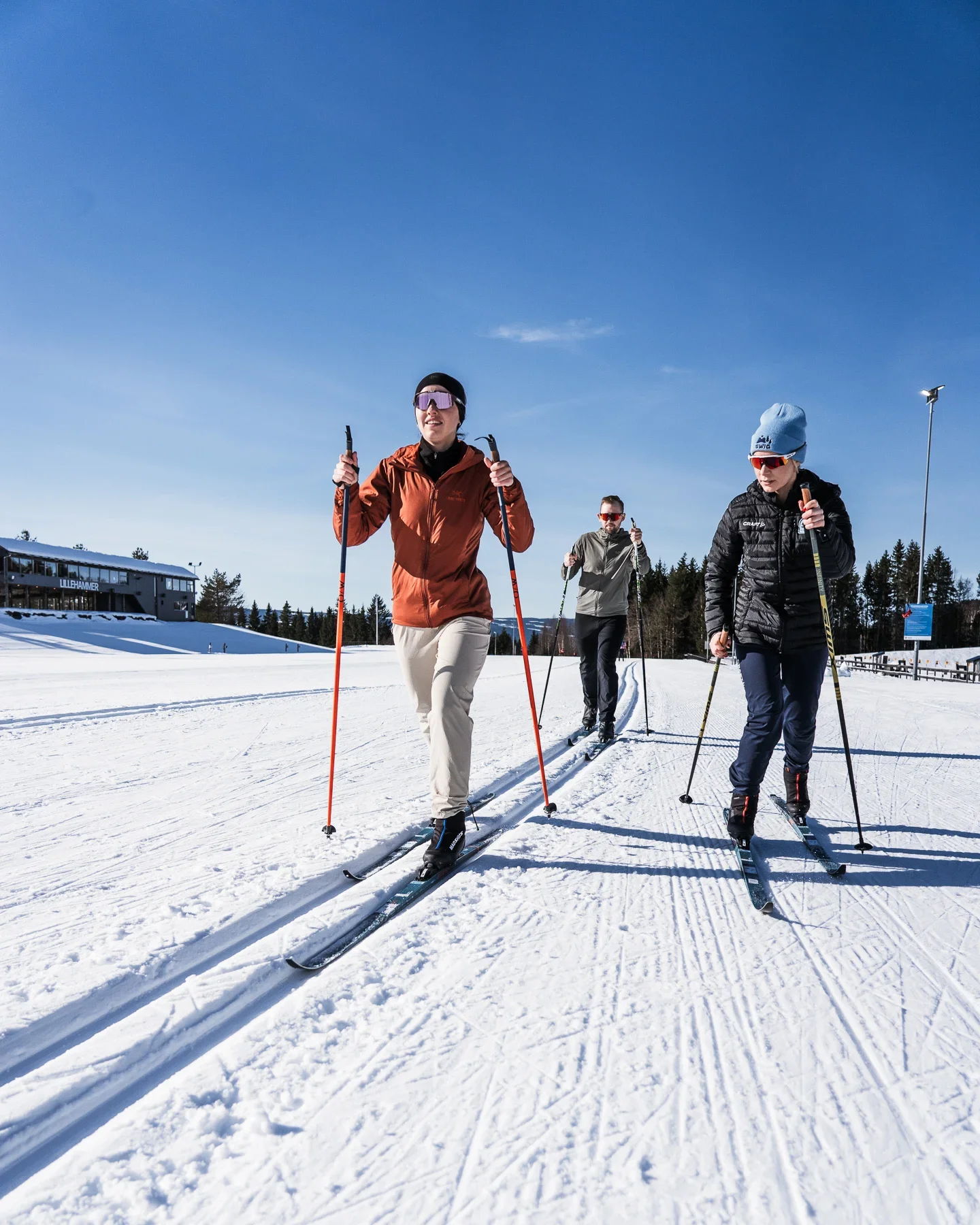 A couple taking cross country skiing lessons. They're skiing in the ski track, while their female teacher skis next to them.