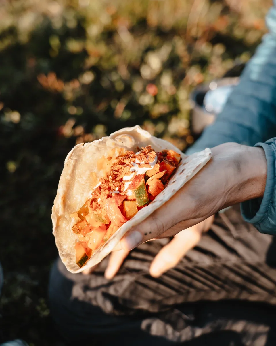A hand holding a wrap with vegetable filling