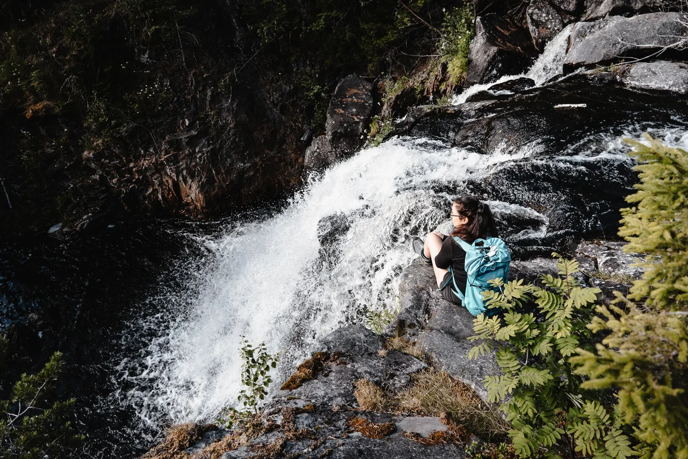 A woman sitting next to the top of a waterfall.