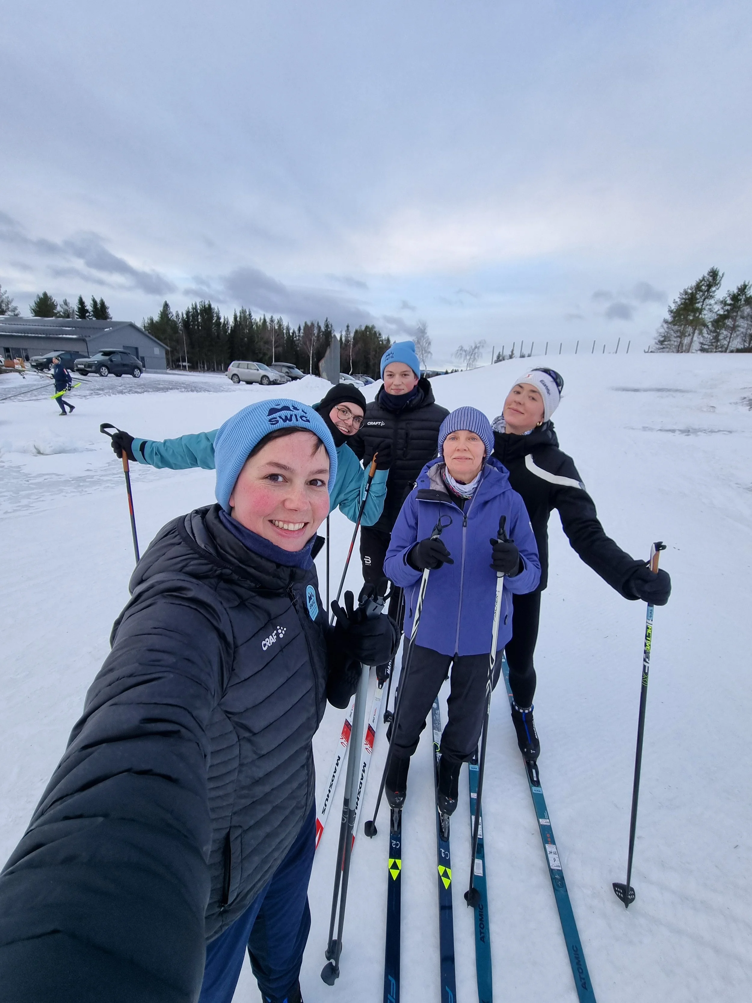 a selfie of a cross person smiling into the camera, in the background you can see 4 people on cross-country skis looking into the camera