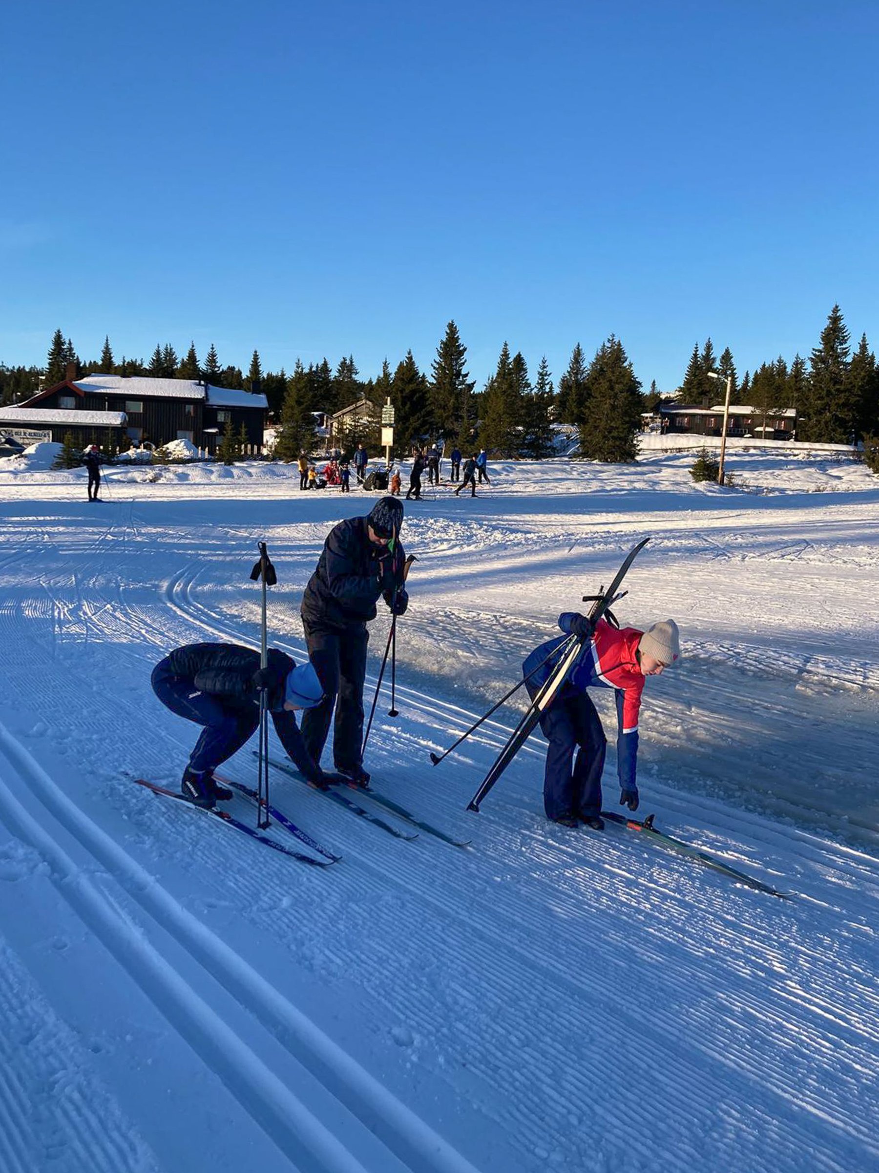 A group of three people standing on a cross-country skiing track getting ready to ski