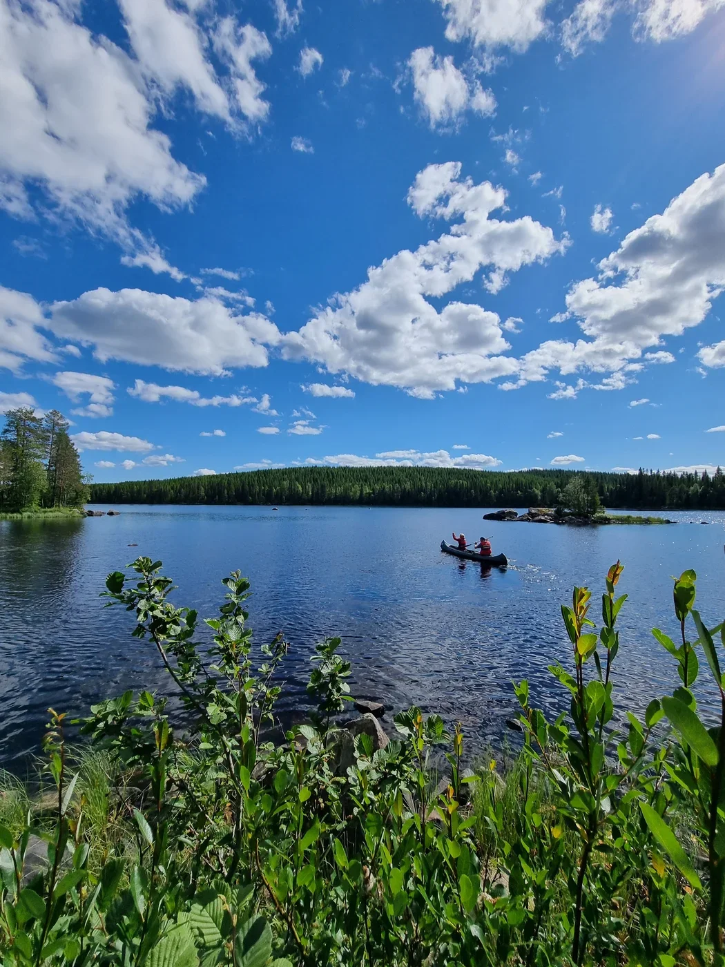A canoe paddling over a blue lake in the sunshine. In the distance hills roll along the shoreline.