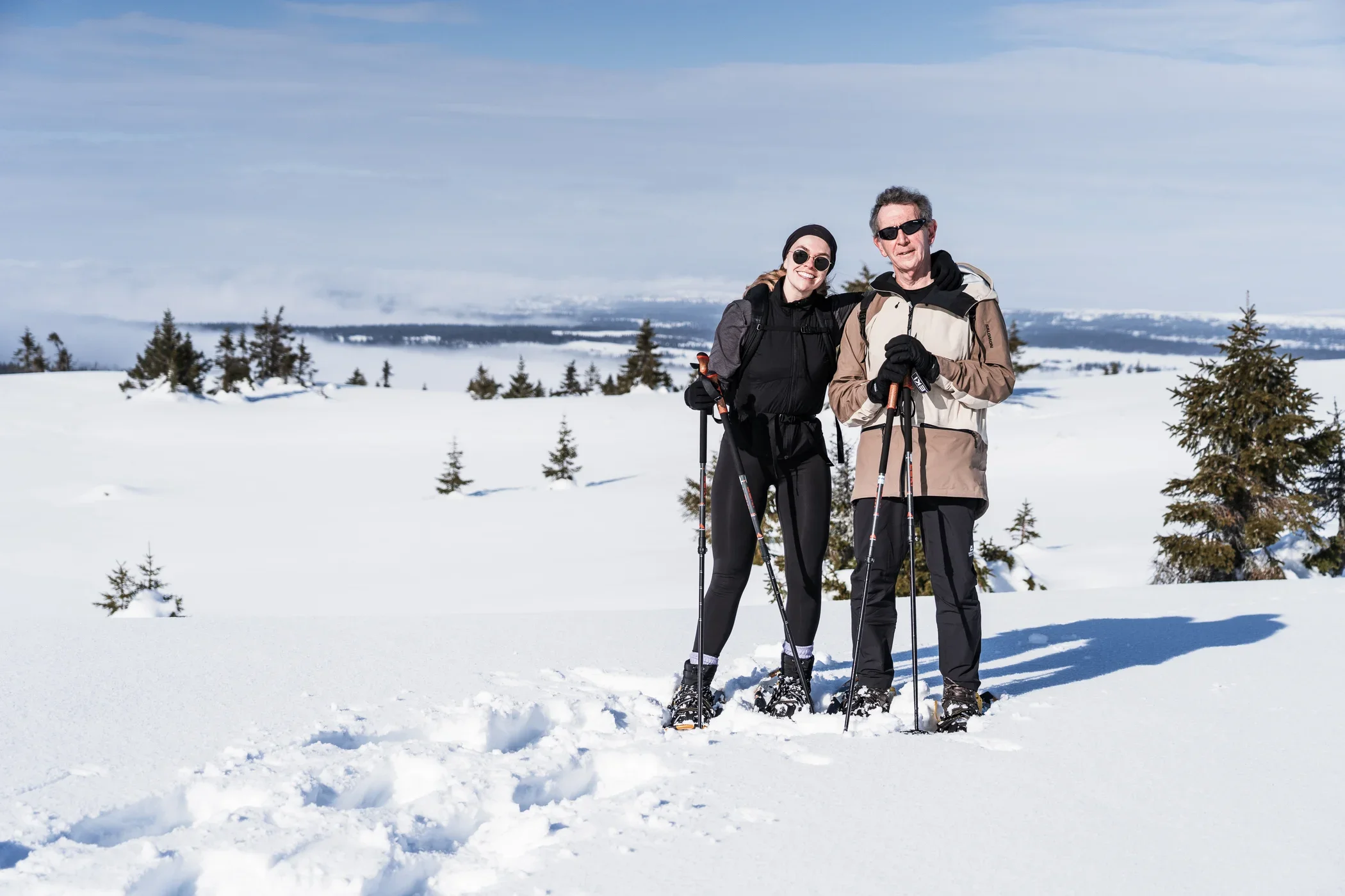 Two people with snowshoes standing in front of a wide winter landscape smiling into the camera