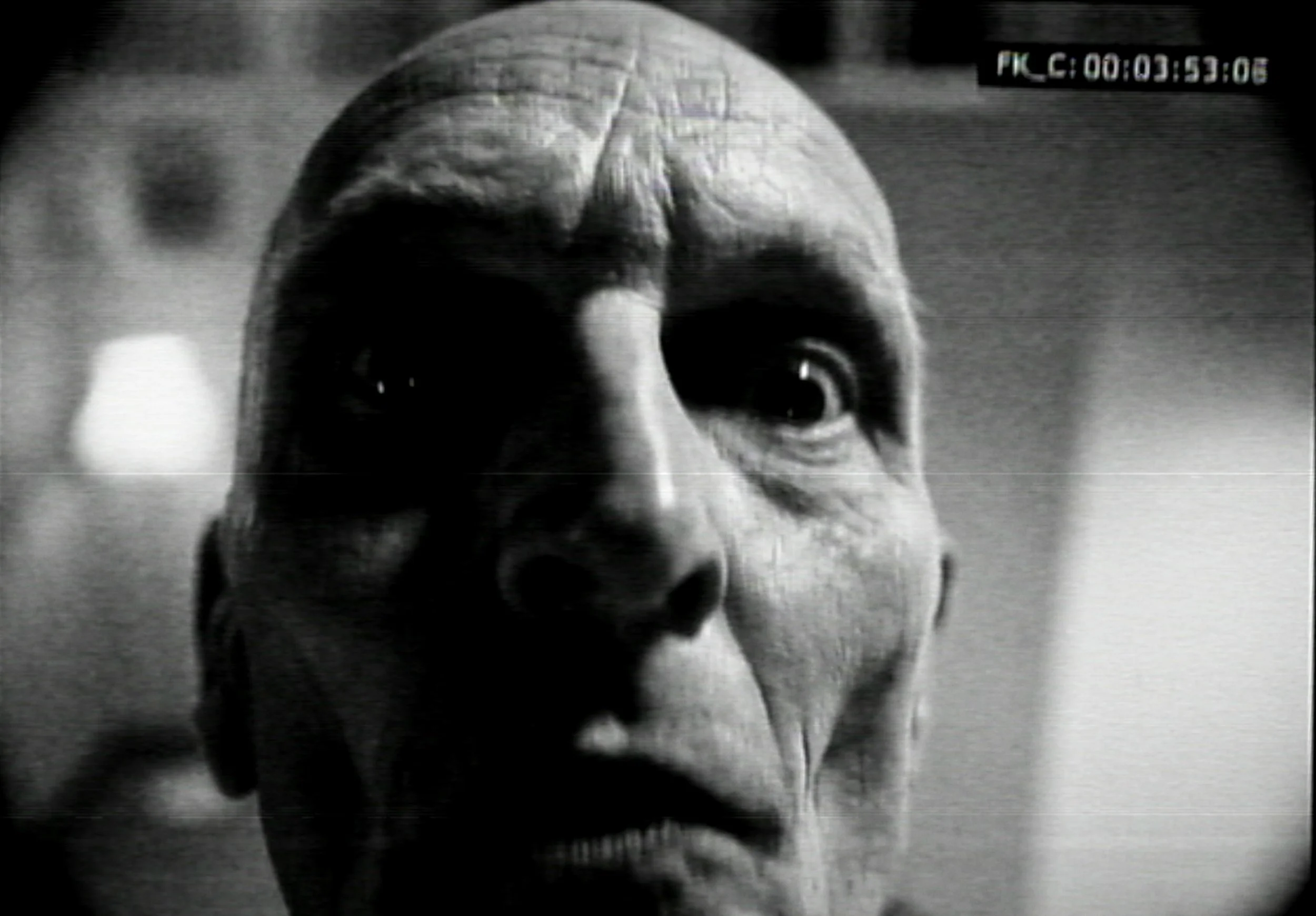 Close-up black and white video shot of a man's face showing age wrinkles, with intense expression and wide-open eyes.