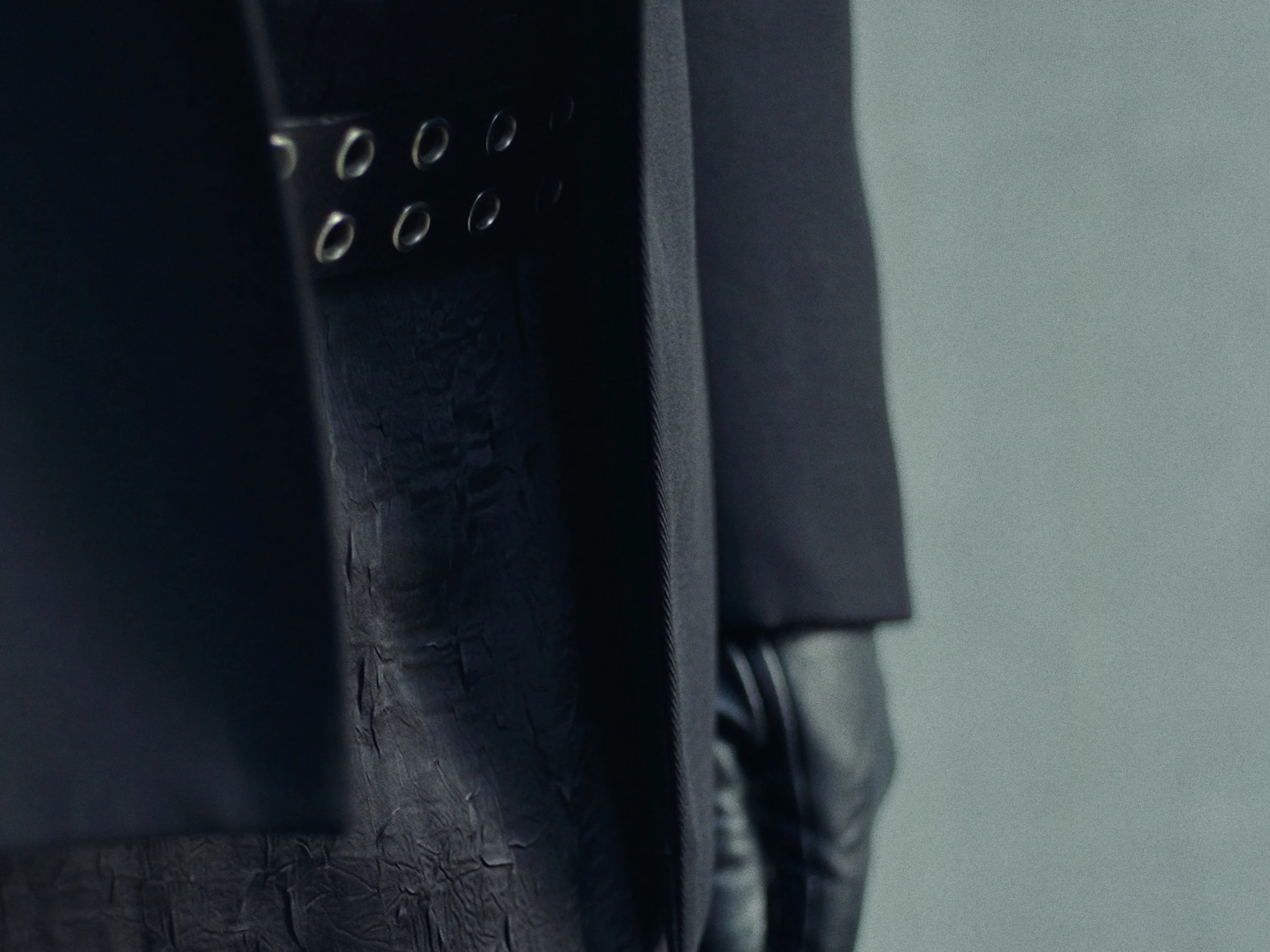 Close-up of a black electronic device, possibly a speaker or radio, with vents or holes, partially obscured by a black fabric or cover.