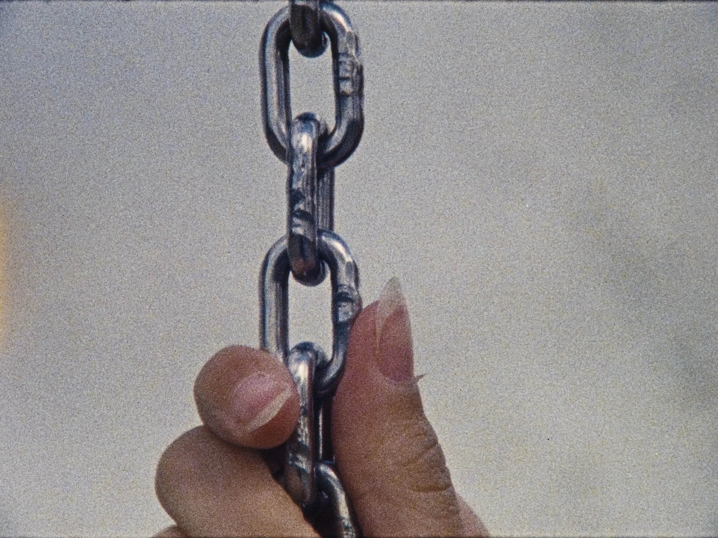 A person's hand holding a metal chain against a plain background.