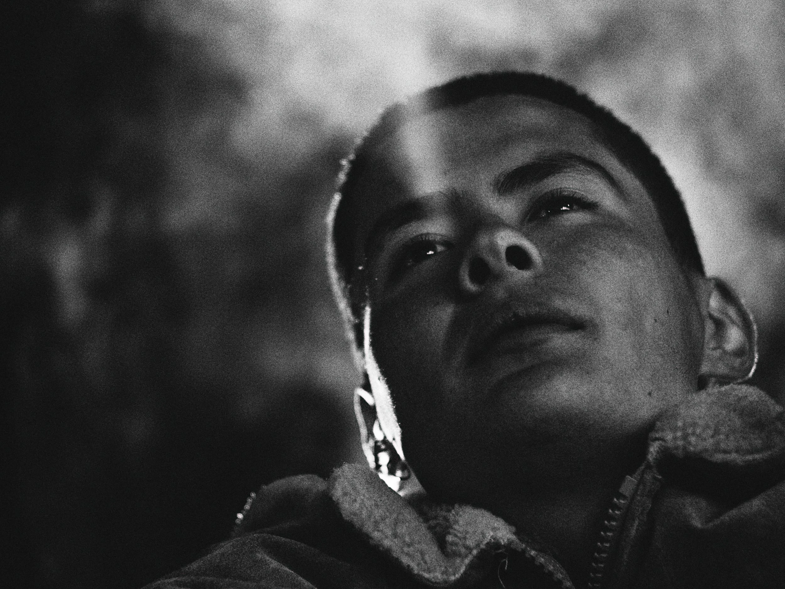 Black and white close-up photo of a young person looking upward, wearing a hoodie with some facial piercings.