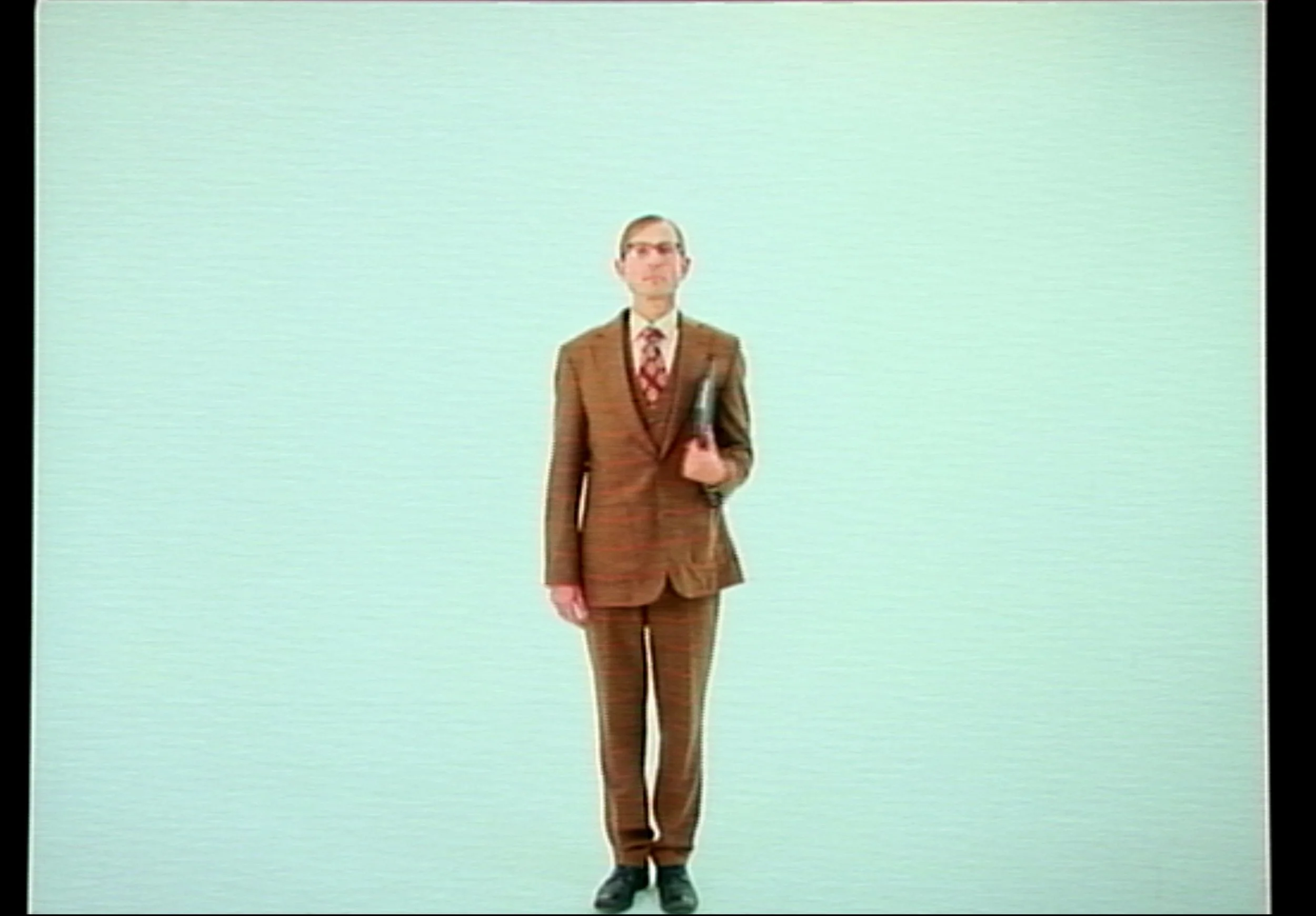 A man in a brown plaid suit standing against a plain, light-colored background, holding a newspaper.