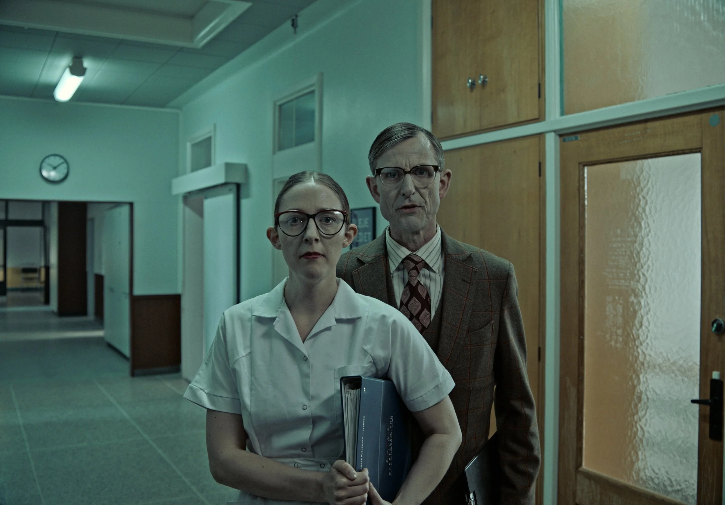 Two professionals, a woman and a man, standing in a hospital hallway.