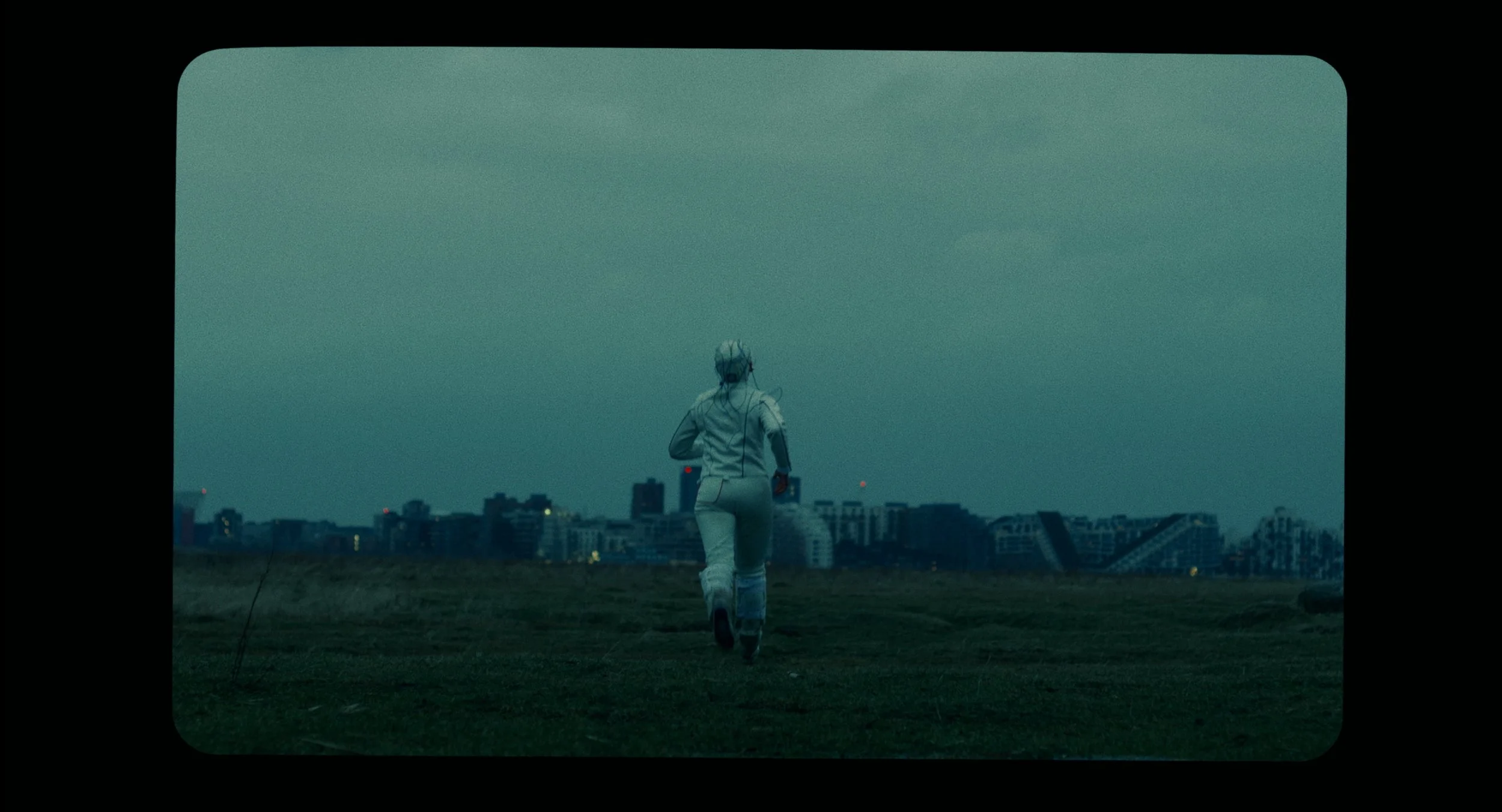 A person dressed in a white spacesuit running on an open field with a cityscape in the background, under a cloudy sky.